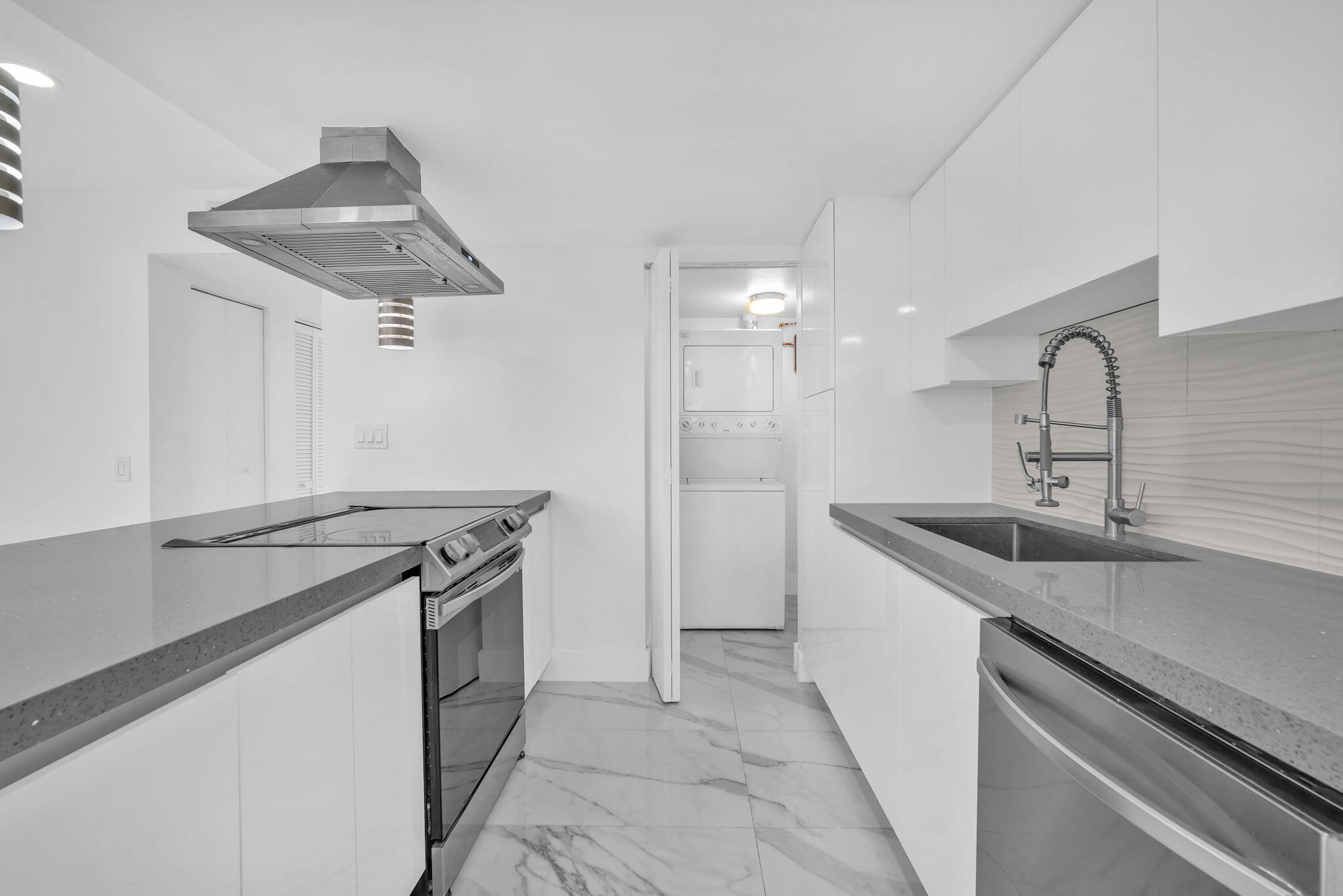 Modern kitchen featuring high-gloss white cabinetry, solid-surface countertops, stone-patterned tile flooring, a stainless steel range hood, and a high-arc pull-down kitchen faucet