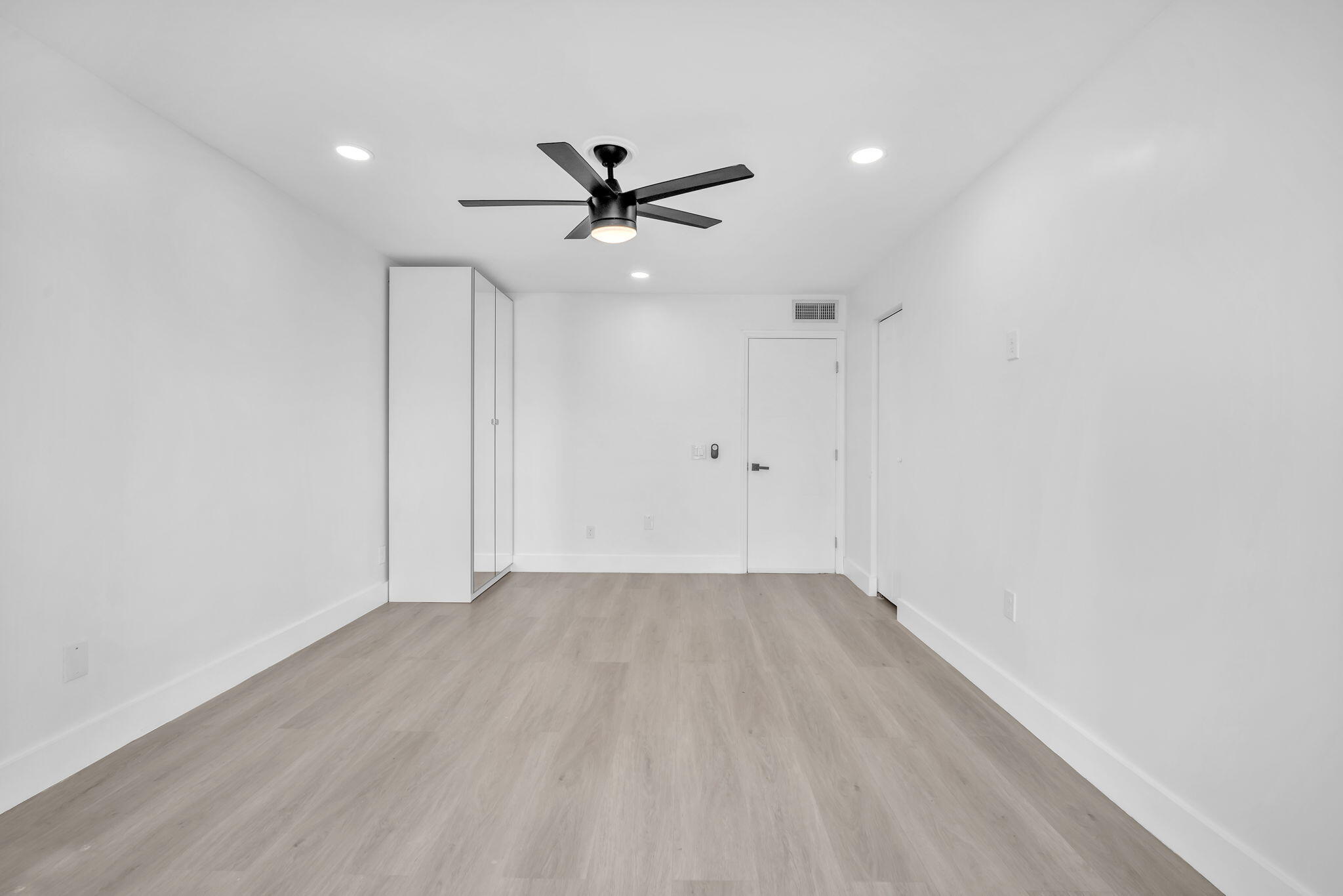 Interior room featuring light-toned wood-finish flooring, recessed lighting, a matte black ceiling fan with integrated light, and built-in floor-to-ceiling cabinetry
