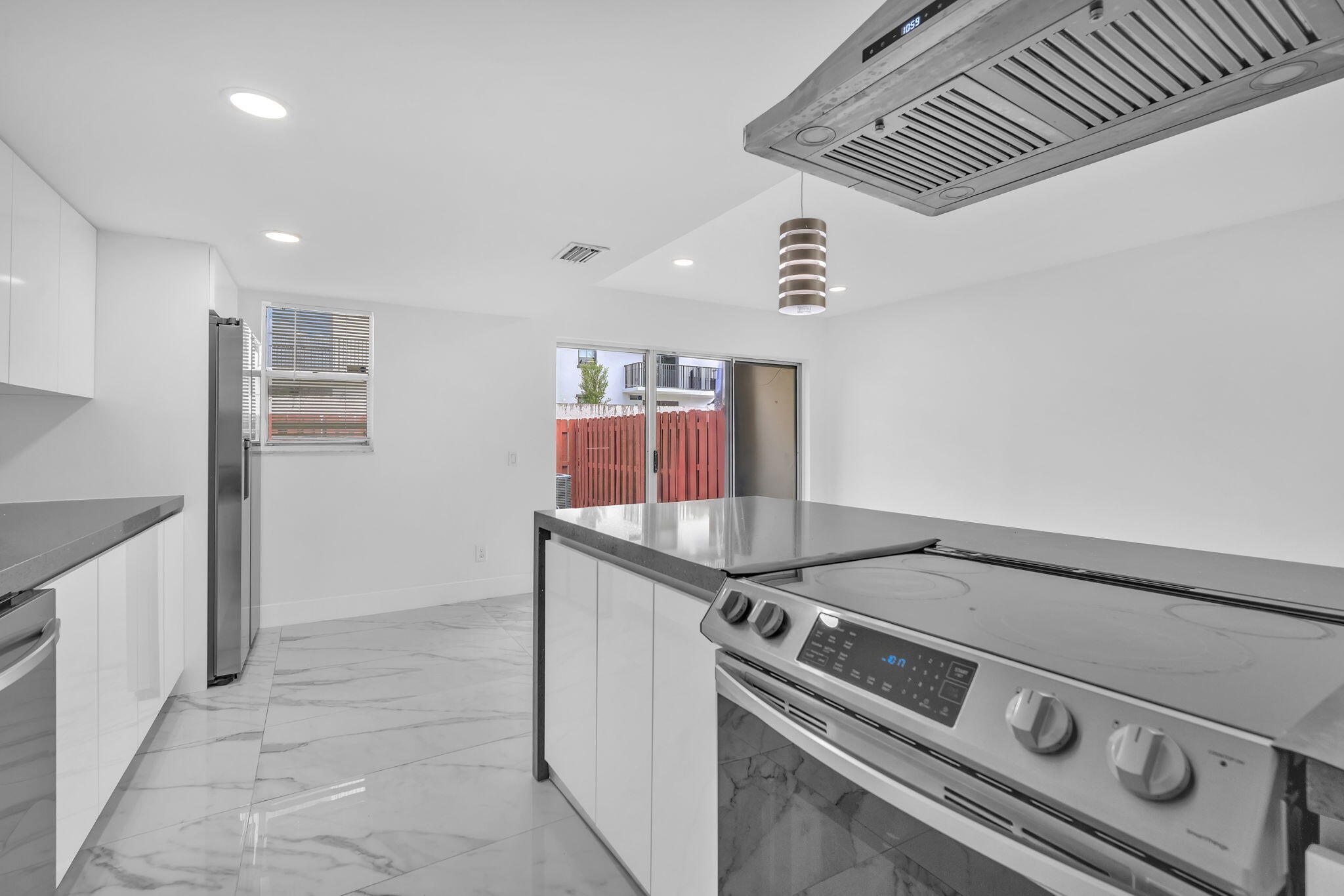 Kitchen featuring high-gloss cabinetry, stone-finish countertops, stainless steel appliances, a ceiling-mounted range hood, and large-format porcelain tile flooring