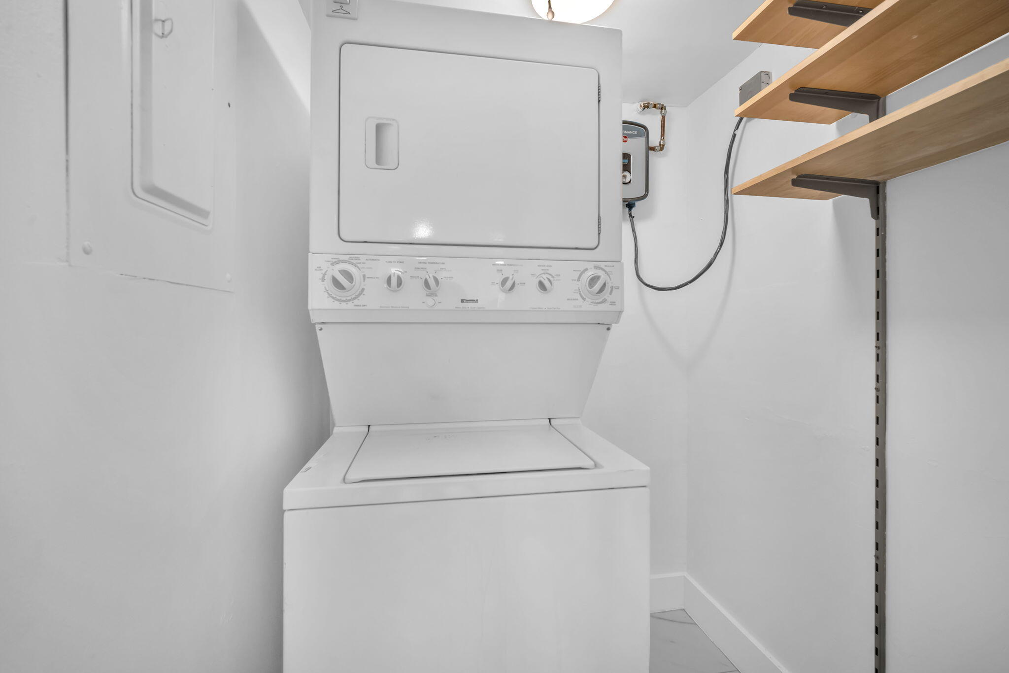 Stacked laundry unit featuring a top-loading washer, dryer, built-in wall shelving, and an tankless electric water heater
