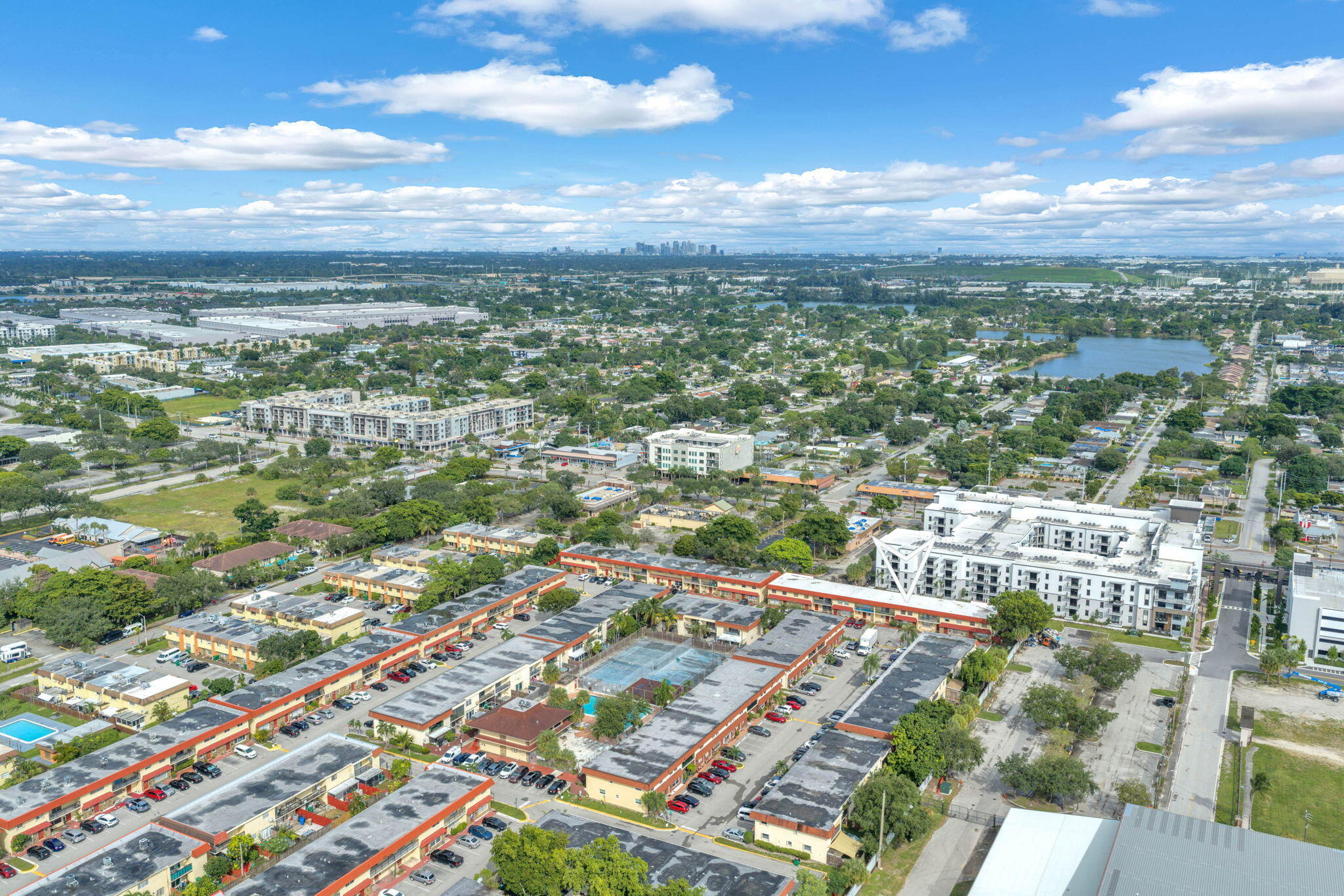 Aerial perspective of a multi-unit complex featuring an on-site swimming pool, designated parking areas, and mature landscaping