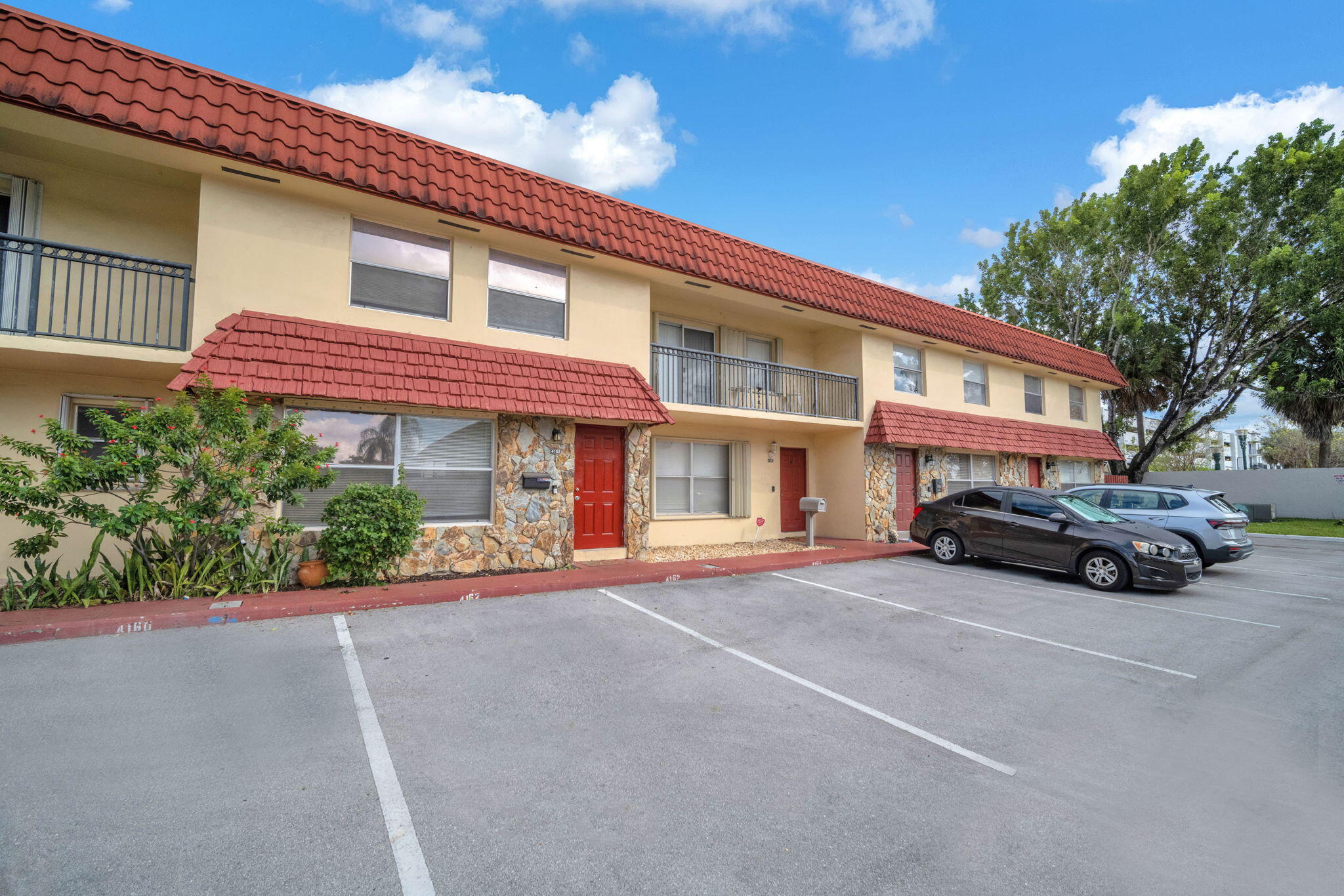 Two-story exterior featuring a Spanish tile roof, stone masonry facade, red entry doors, and metal balcony railings