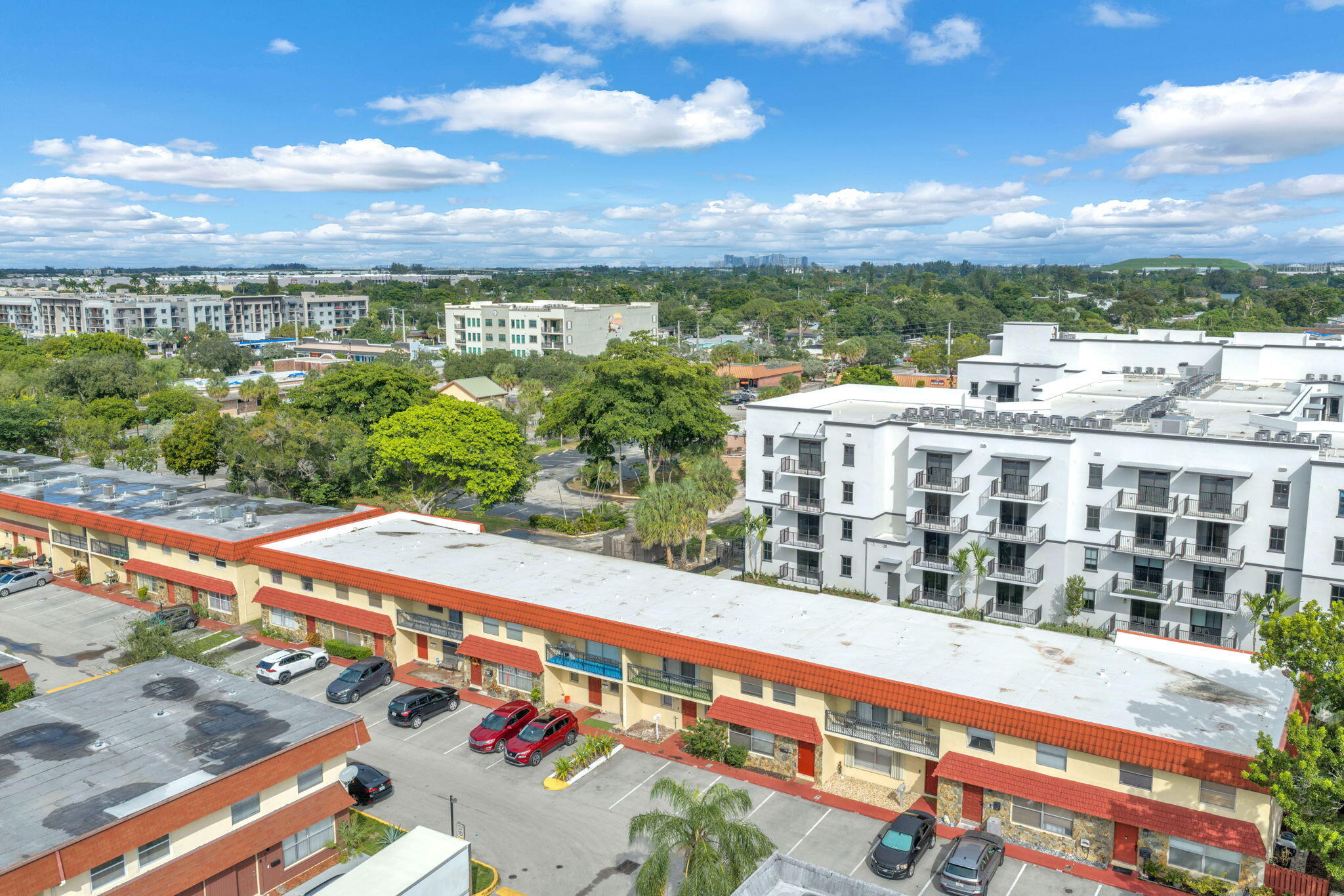 Aerial perspective of a multi-unit complex featuring terra-cotta style roofing, exterior staircases, integrated balconies, and designated surface parking