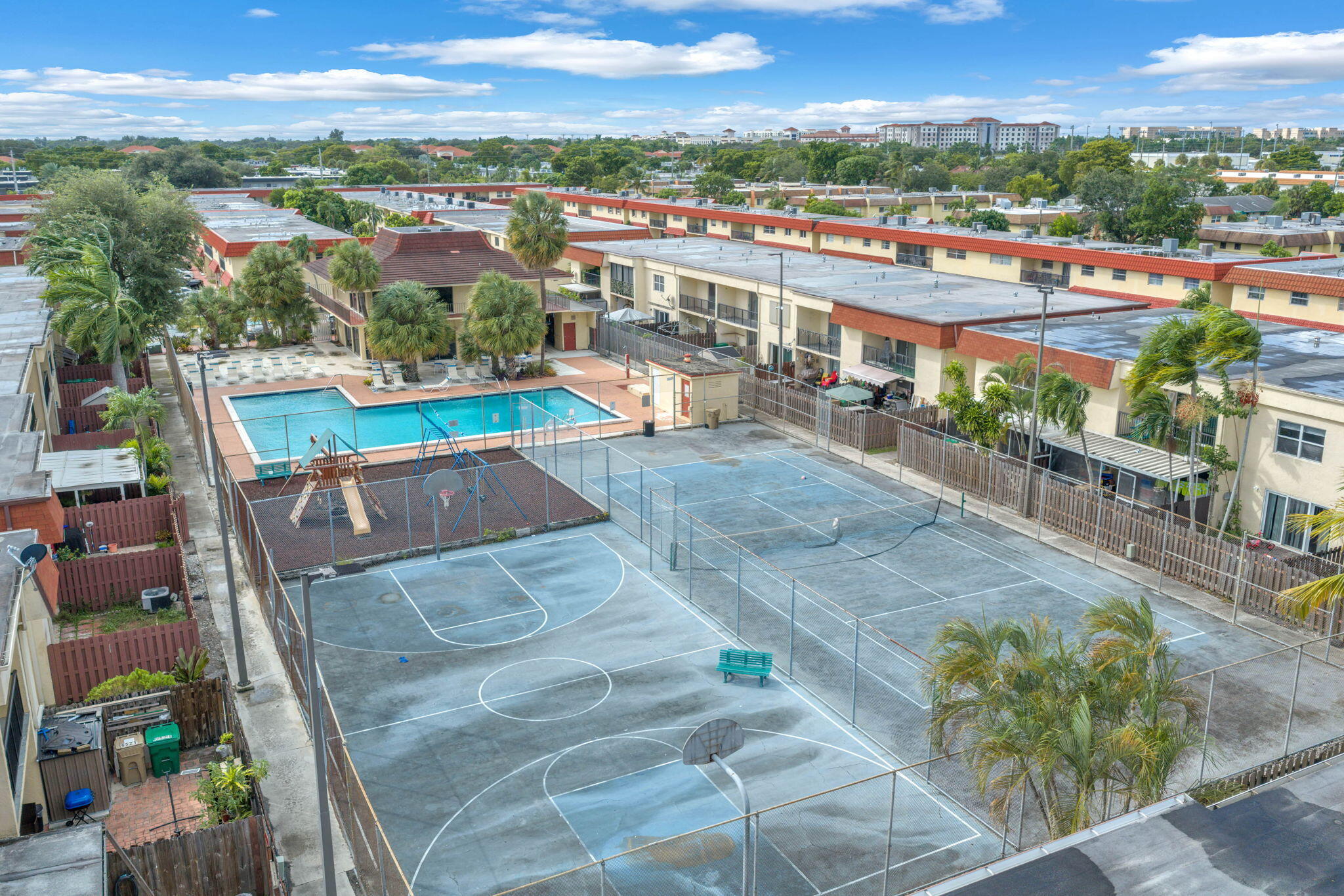 Community recreation area featuring a swimming pool, fenced basketball court, tennis court, and play structure