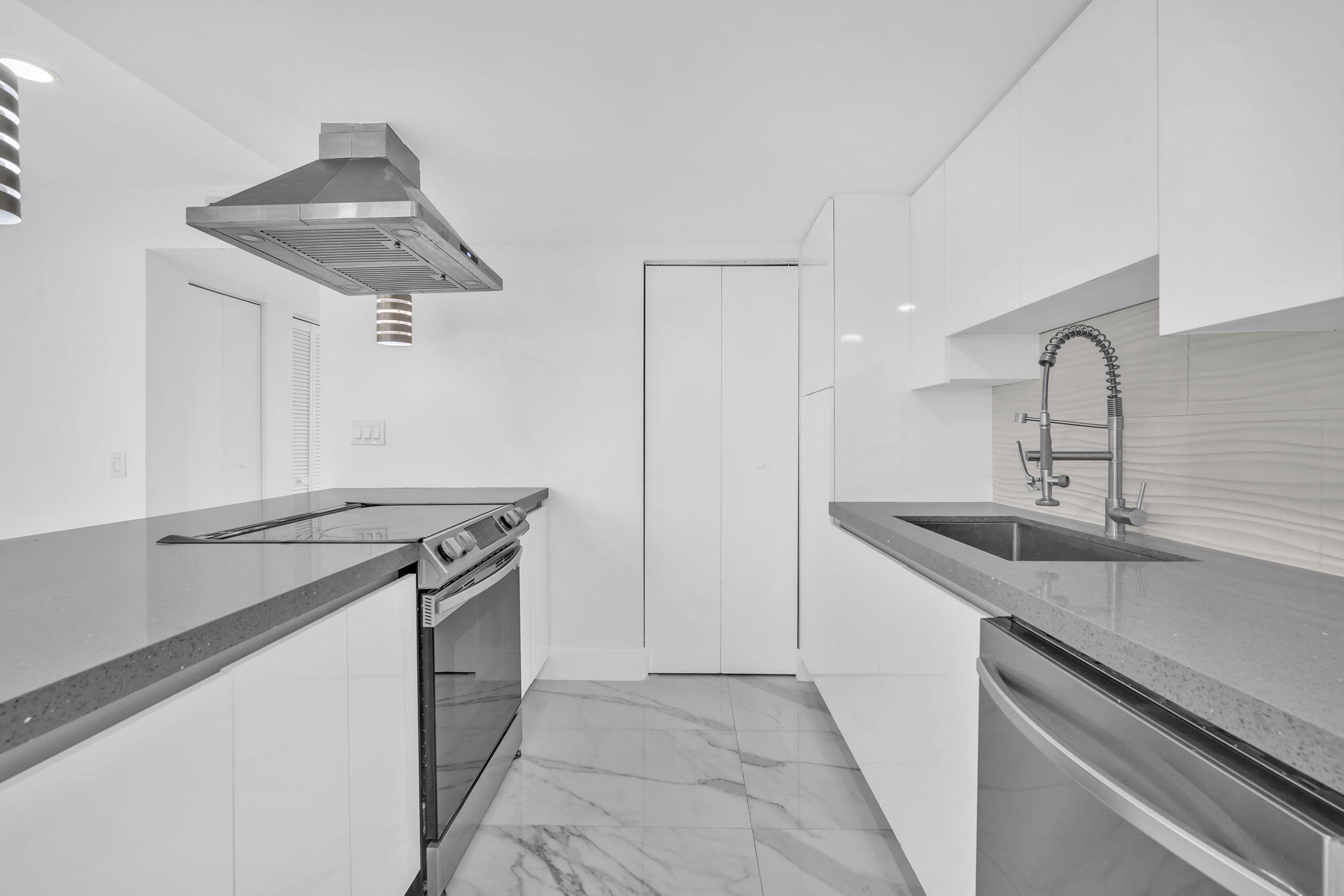 Contemporary kitchen featuring sleek white cabinetry, stone-finish countertops, stainless steel appliances, a professional-style range hood, and large-format tile flooring
