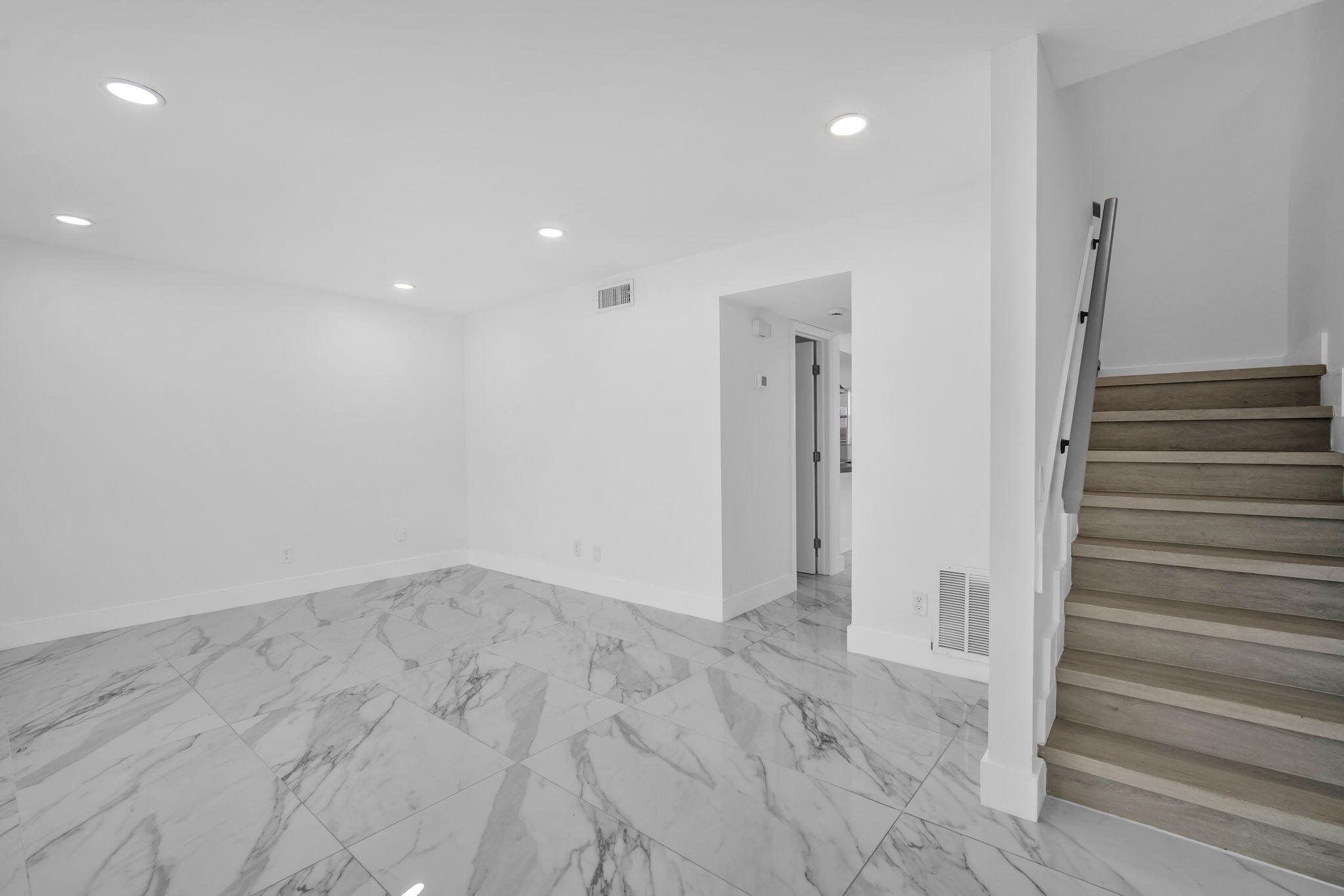 Large-format stone-style tile flooring, recessed ceiling lighting, and staircase featuring wood-finish treads and a metal handrail