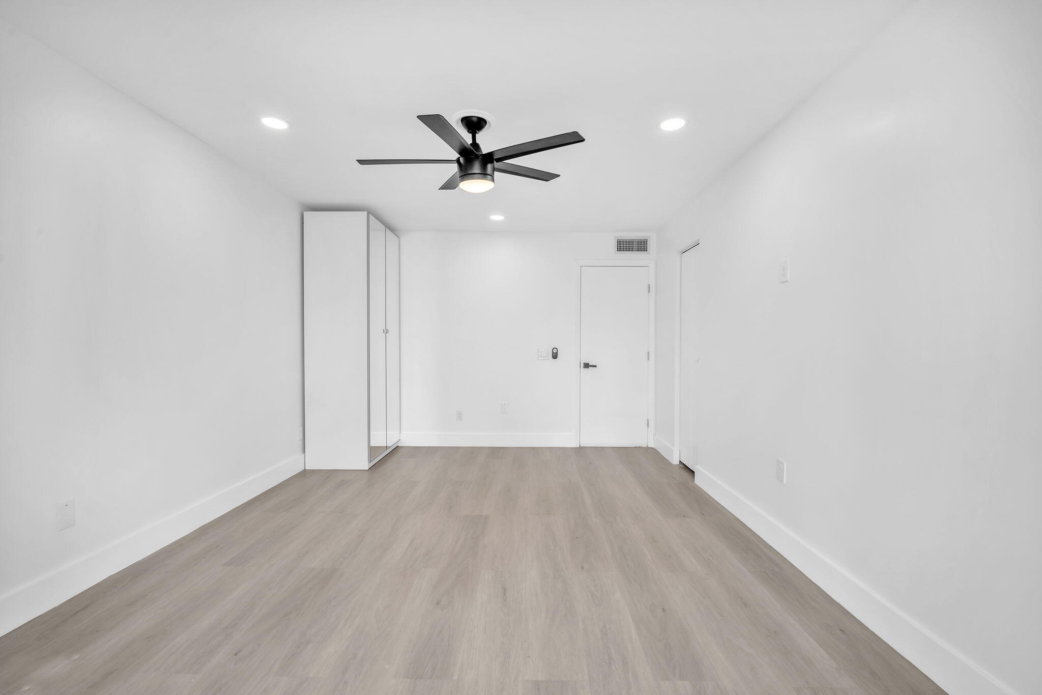 Neutral-toned wood-finish flooring, recessed lighting, matte black ceiling fan, and floor-to-ceiling built-in cabinetry