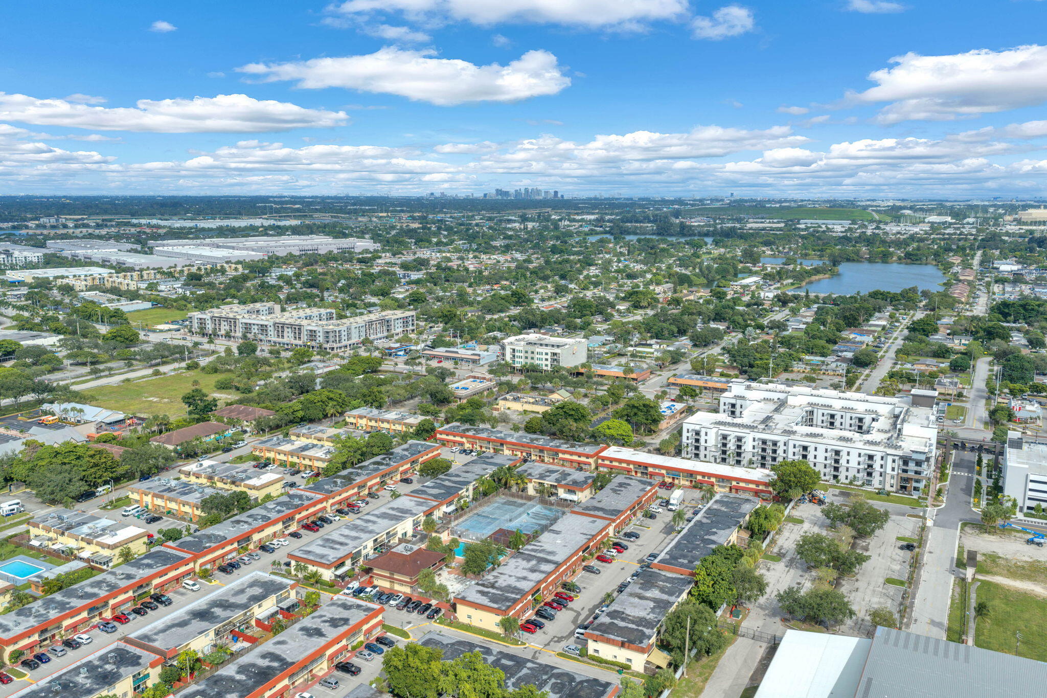 Aerial perspective featuring multi-unit complexes, paved parking areas, and a central tennis court within the property grounds