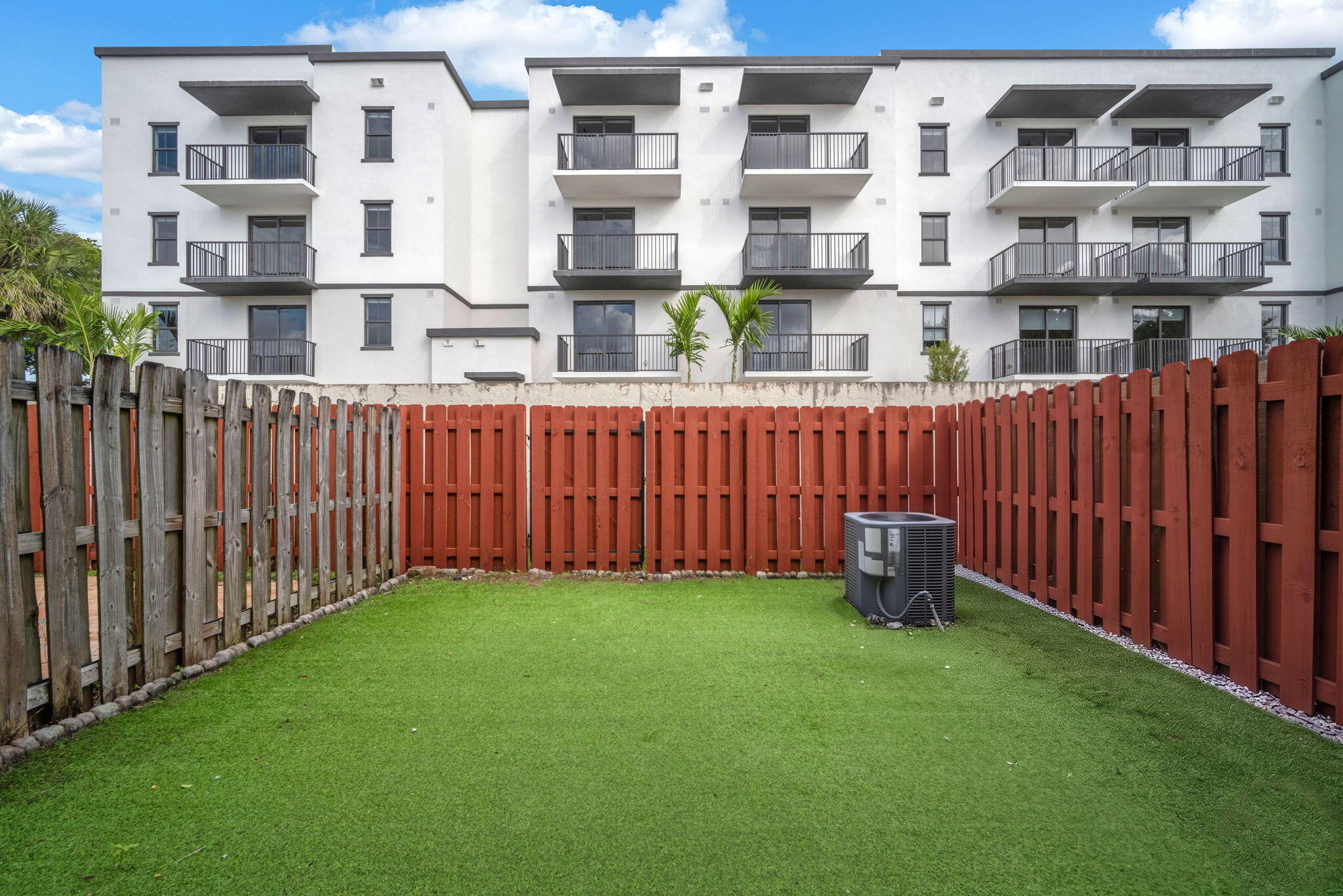 Fenced backyard featuring synthetic turf, wood privacy fencing, and an exterior HVAC unit