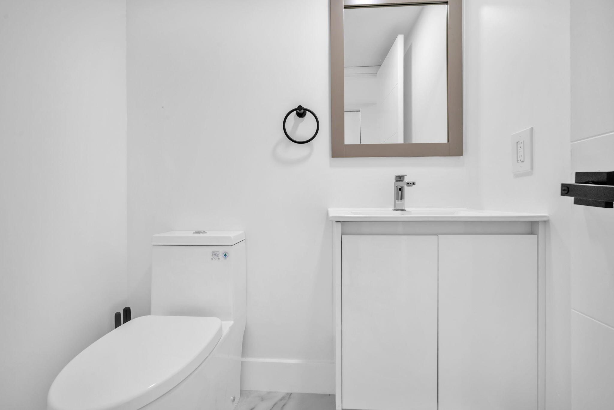 Bathroom featuring a white vanity cabinet, rectangular countertop sink, wall-mounted circular towel ring, and a framed mirror