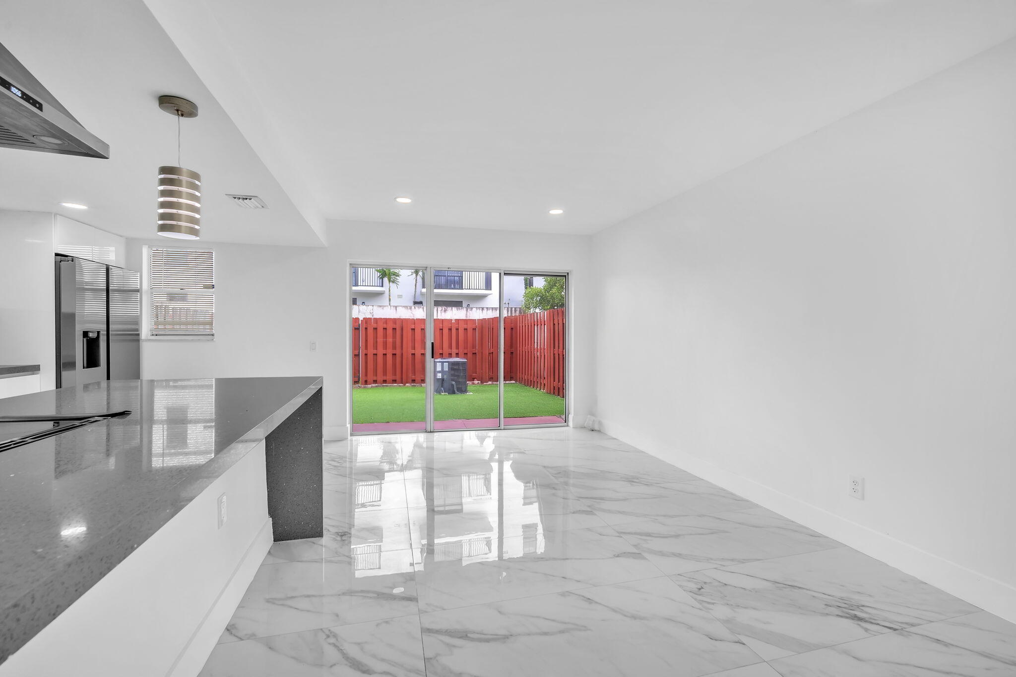 Open-concept interior featuring large-format tile flooring, quartz waterfall kitchen island, sliding glass doors, recessed lighting, and a fenced exterior patio area