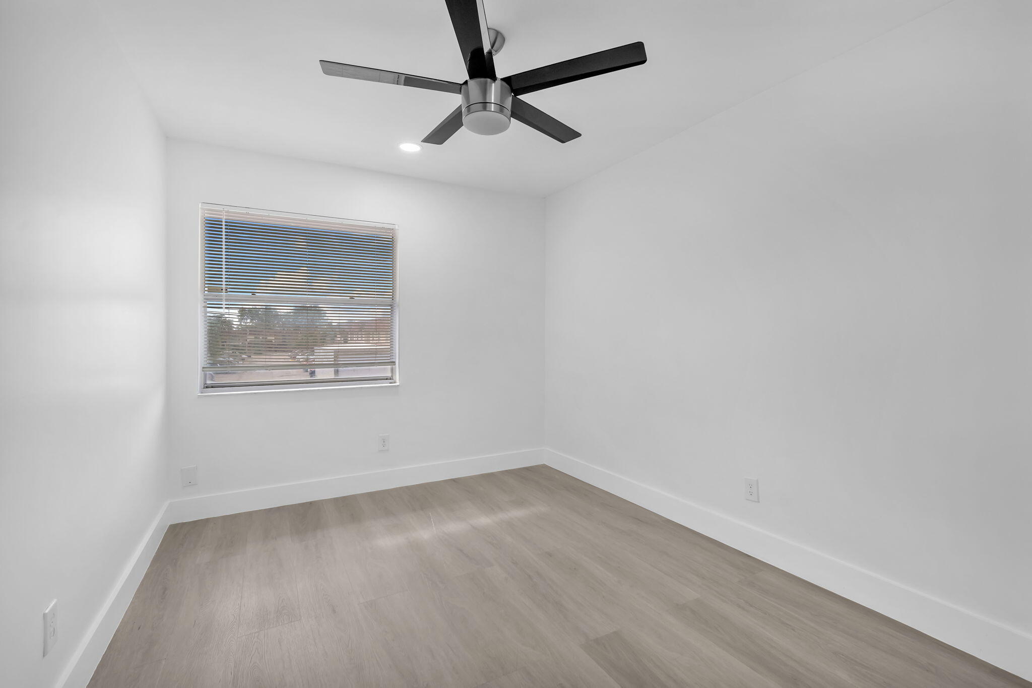 Neutral interior space featuring wood-finish flooring, a contemporary brushed-metal ceiling fan, and a single-hung window with installed blinds