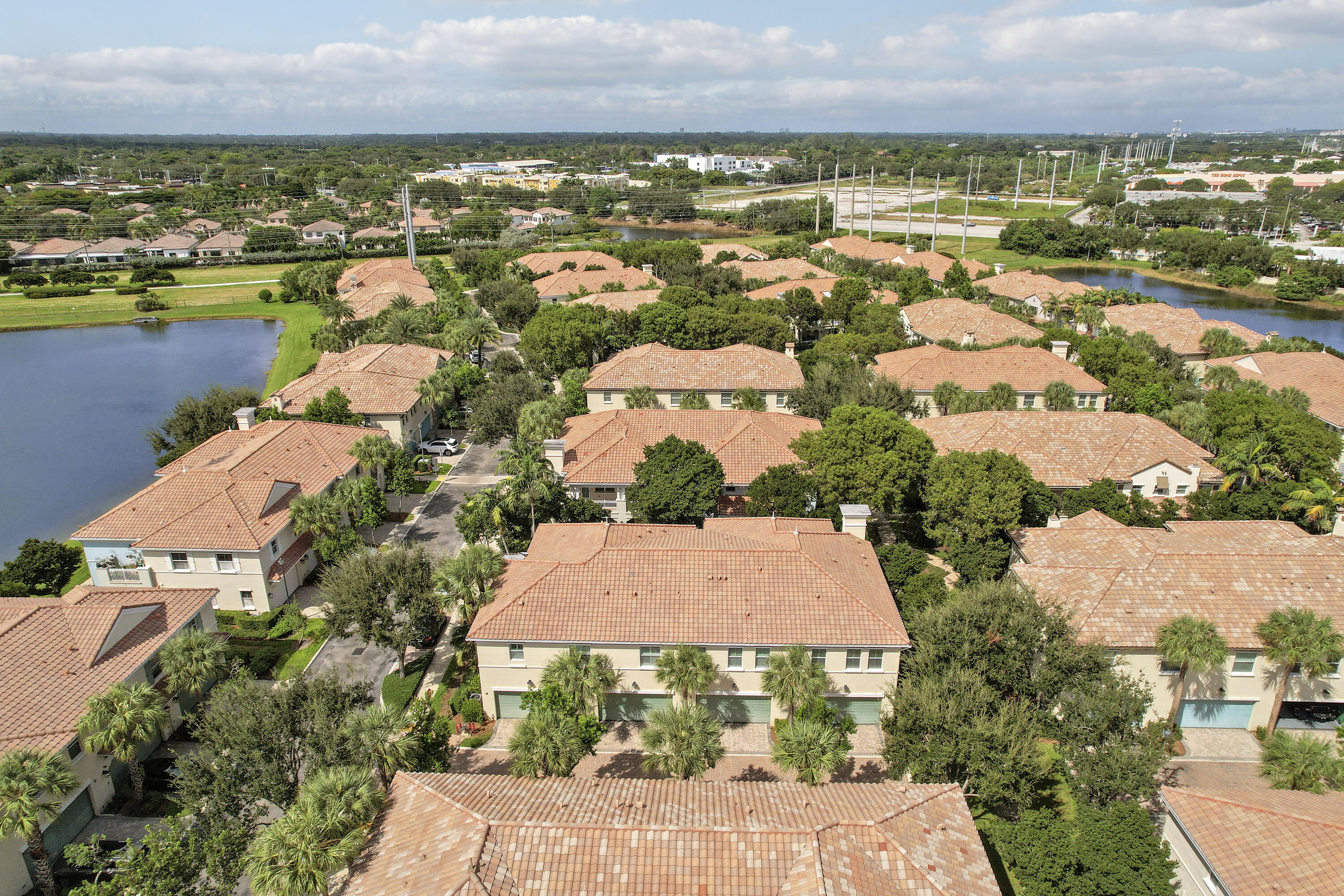 Aerial perspective of a multi-unit residential complex featuring clay tile roofing, light-toned stucco exteriors, attached multi-car garages, and surrounding waterfront scenery Aerial perspective of a multi-unit residential complex featuring clay tile roofing, light-toned stucco exteriors, attached multi-car garages, and surrounding waterfront scenery