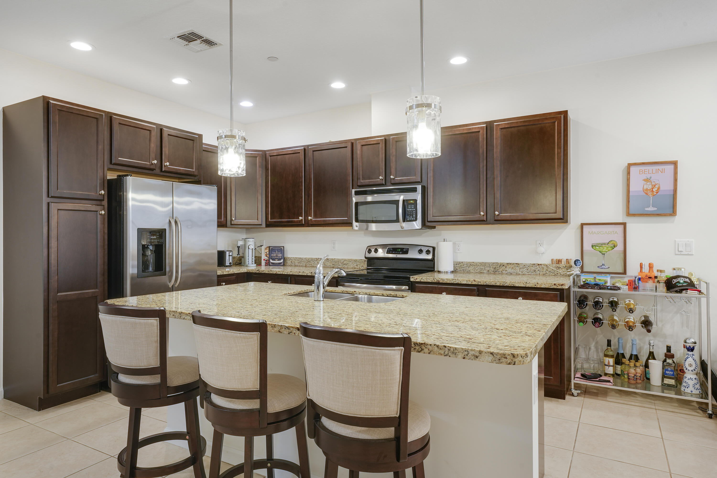 Kitchen featuring dark wood cabinetry, stone countertops, stainless steel appliances, a central island with an integrated sink, and recessed ceiling lighting