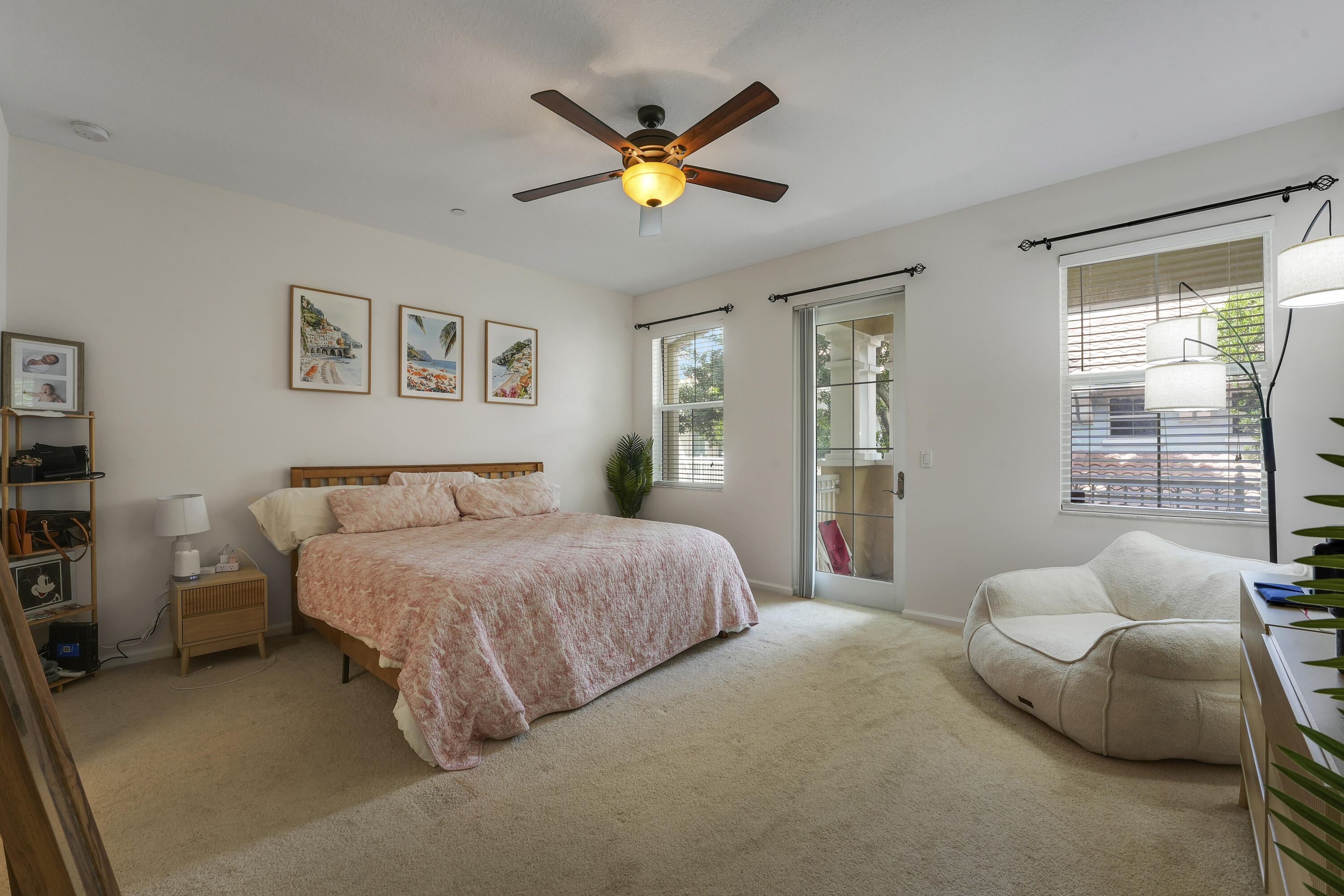 Neutral-toned interior featuring wall-to-wall carpeting, a ceiling fan with integrated lighting, multiple windows with horizontal blinds, and a glass-paneled exterior door