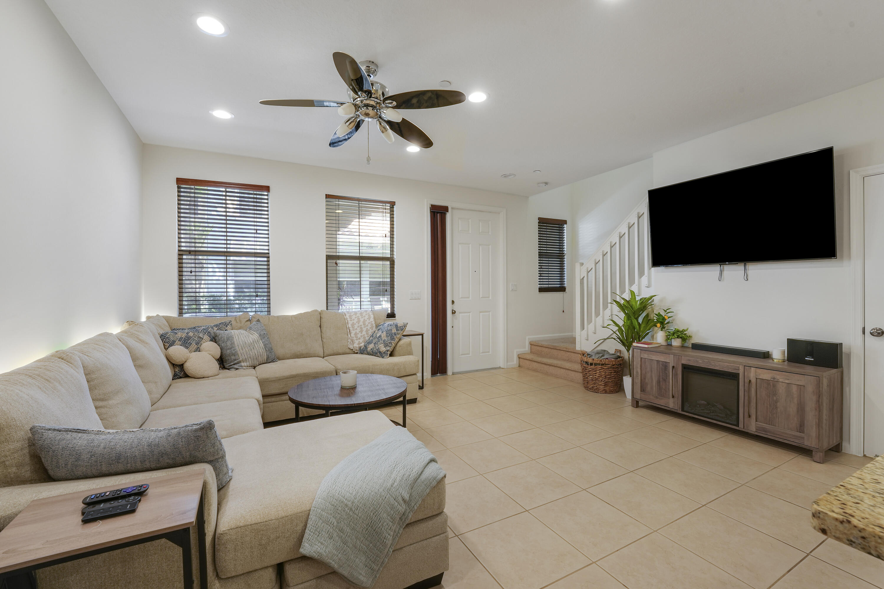 Living area featuring neutral tile flooring, recessed ceiling lighting, a multi-blade ceiling fan, and staircase with white vertical balusters