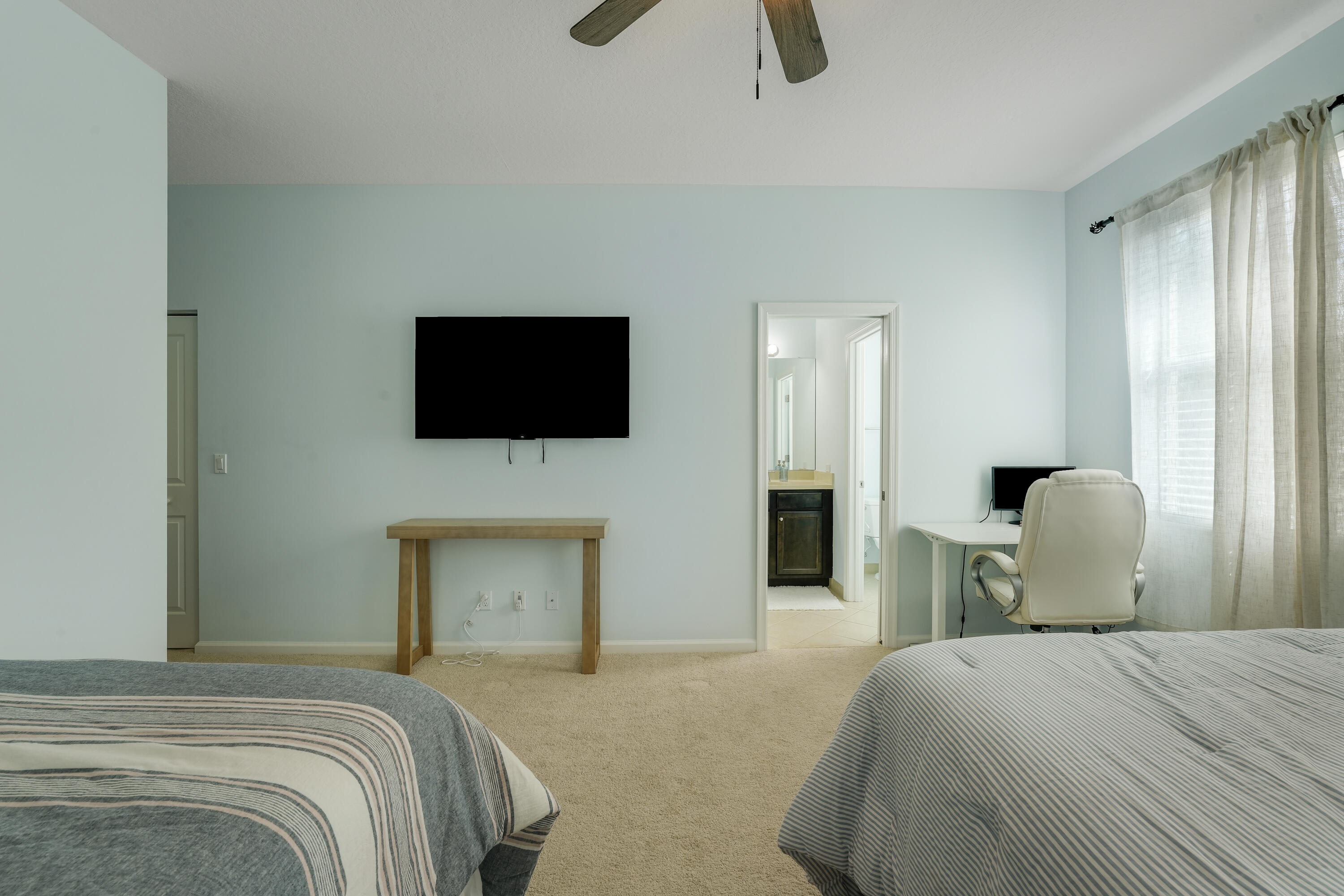 Neutral-toned carpeted flooring, ceiling fan with light fixture, and windows with drapery hardware