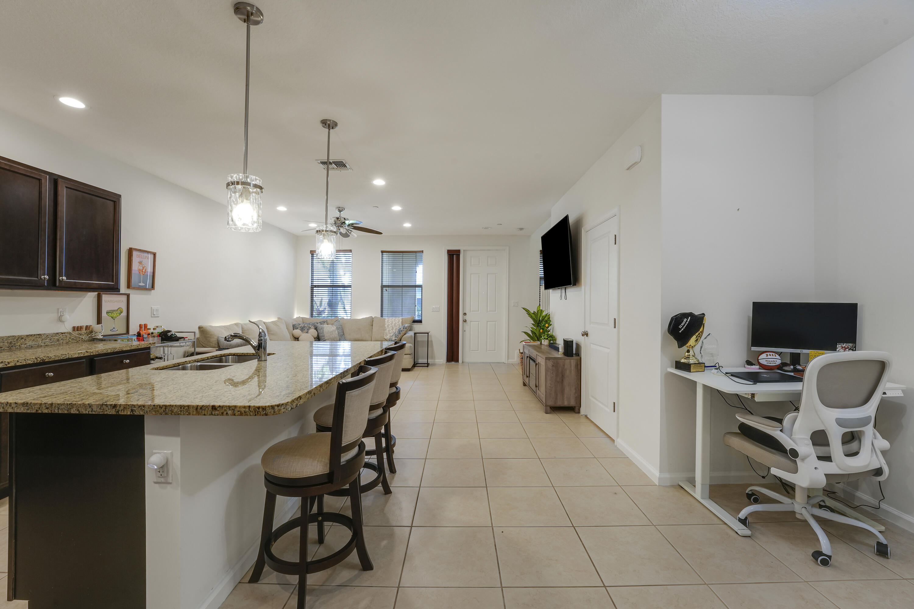 Kitchen featuring dark cabinetry, stone-surface countertops, central island with double-basin sink, pendant lighting, and tile flooring