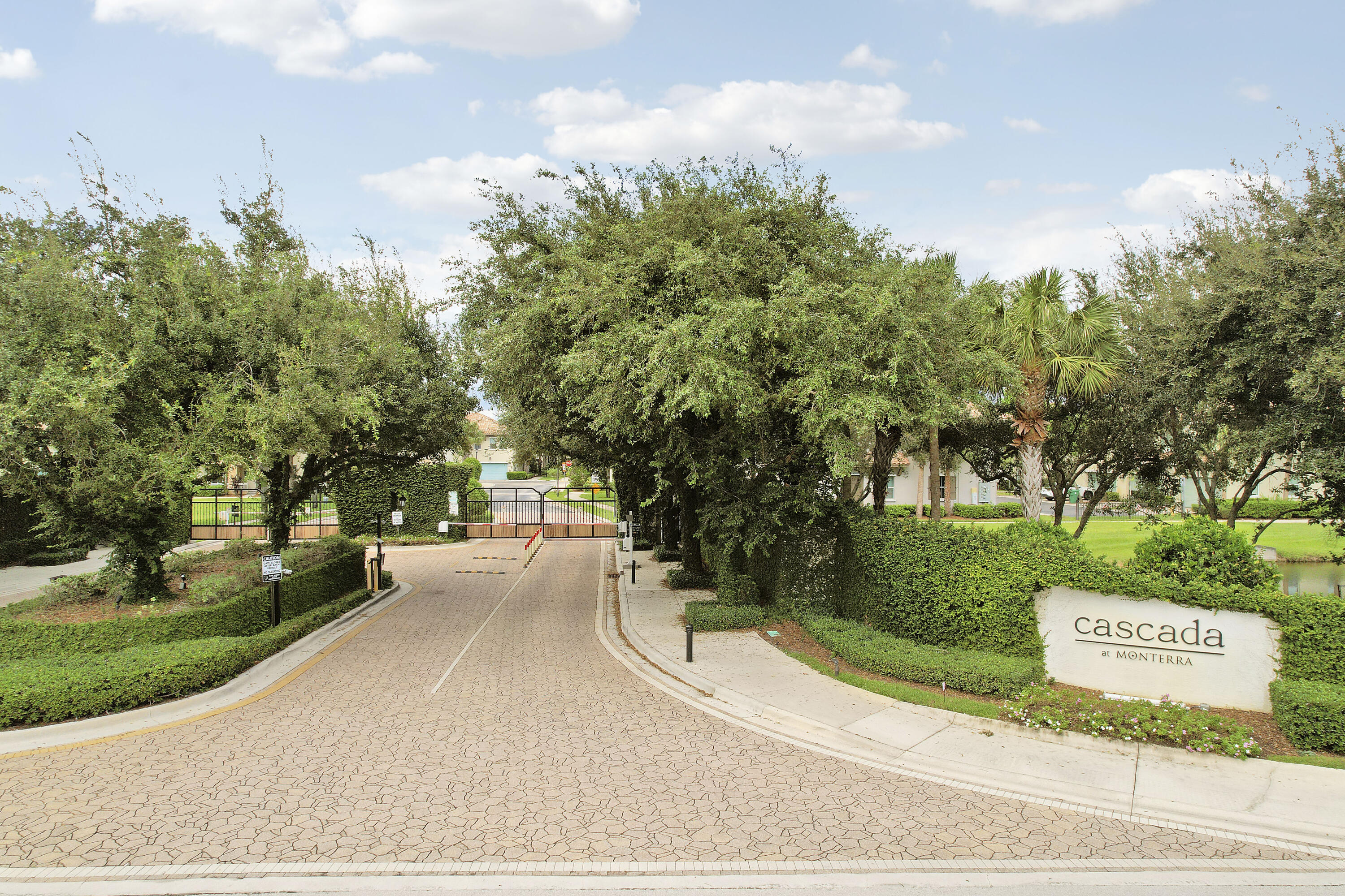 Gated entrance featuring decorative paver driveway, manicured landscaping, and mature trees