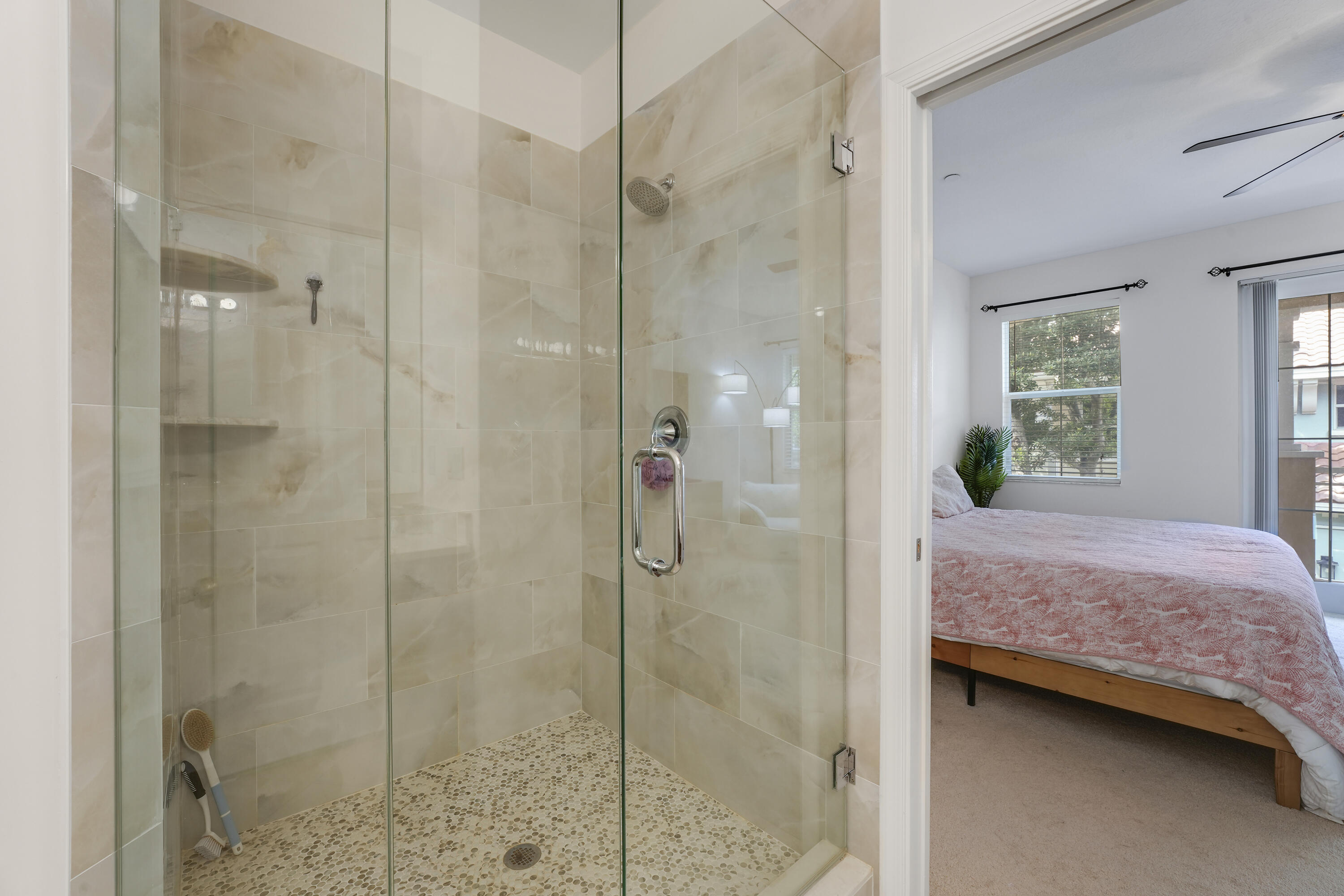 Walk-in shower featuring a glass enclosure, wall-mounted shower head, built-in shelving, and stone-finish floor tiling