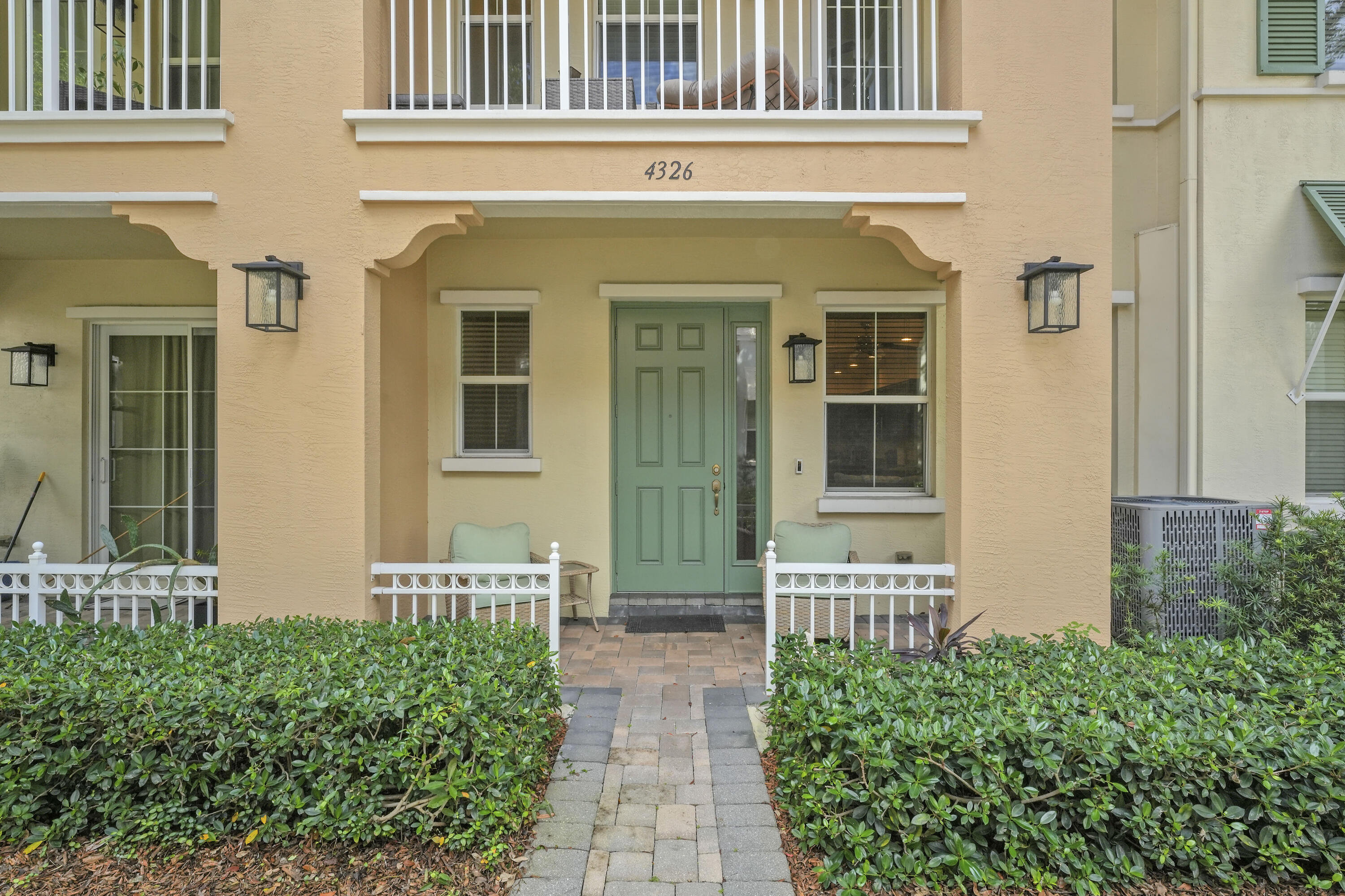Covered entryway featuring a paver walkway, green six-panel door with sidelight, decorative exterior corbels, and wall-mounted lantern fixtures