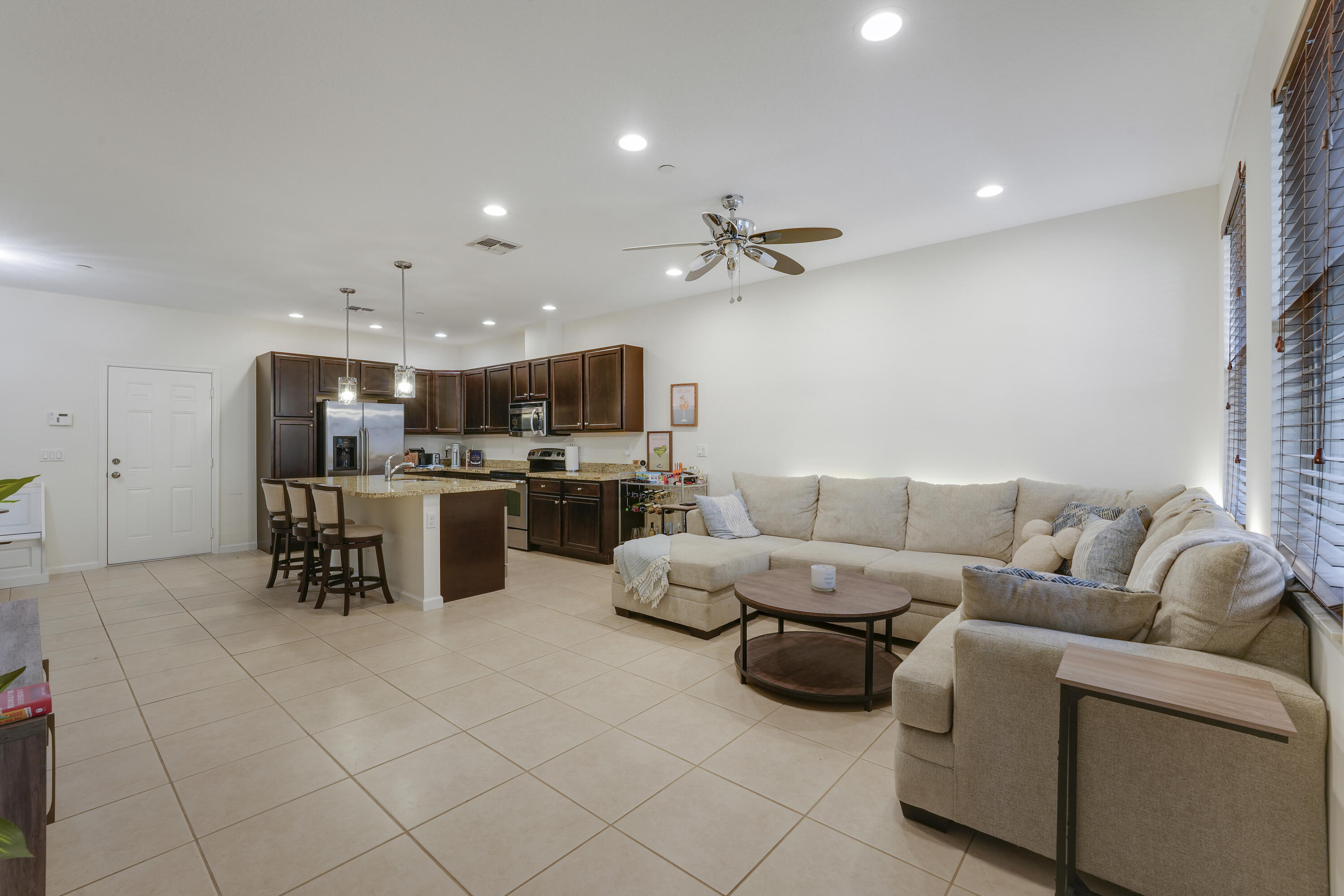 Open-concept interior featuring large-format tile flooring, recessed ceiling lighting, kitchen island with stone countertop, dark wood cabinetry, and a ceiling fan