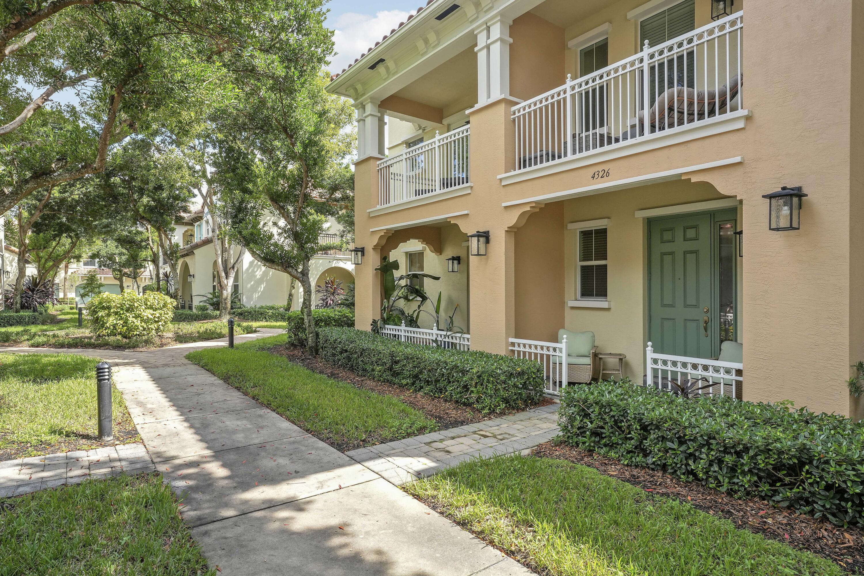 Two-story exterior featuring a stucco facade, covered balconies with white railings, a front porch, and manicured landscaping