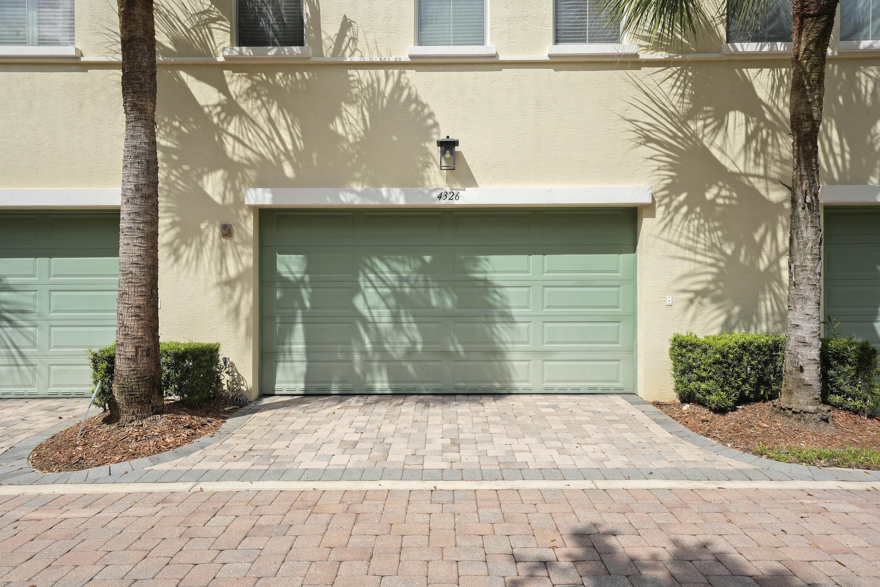 Stucco exterior featuring a multi-panel garage door, decorative exterior wall sconce, and paver stone driveway