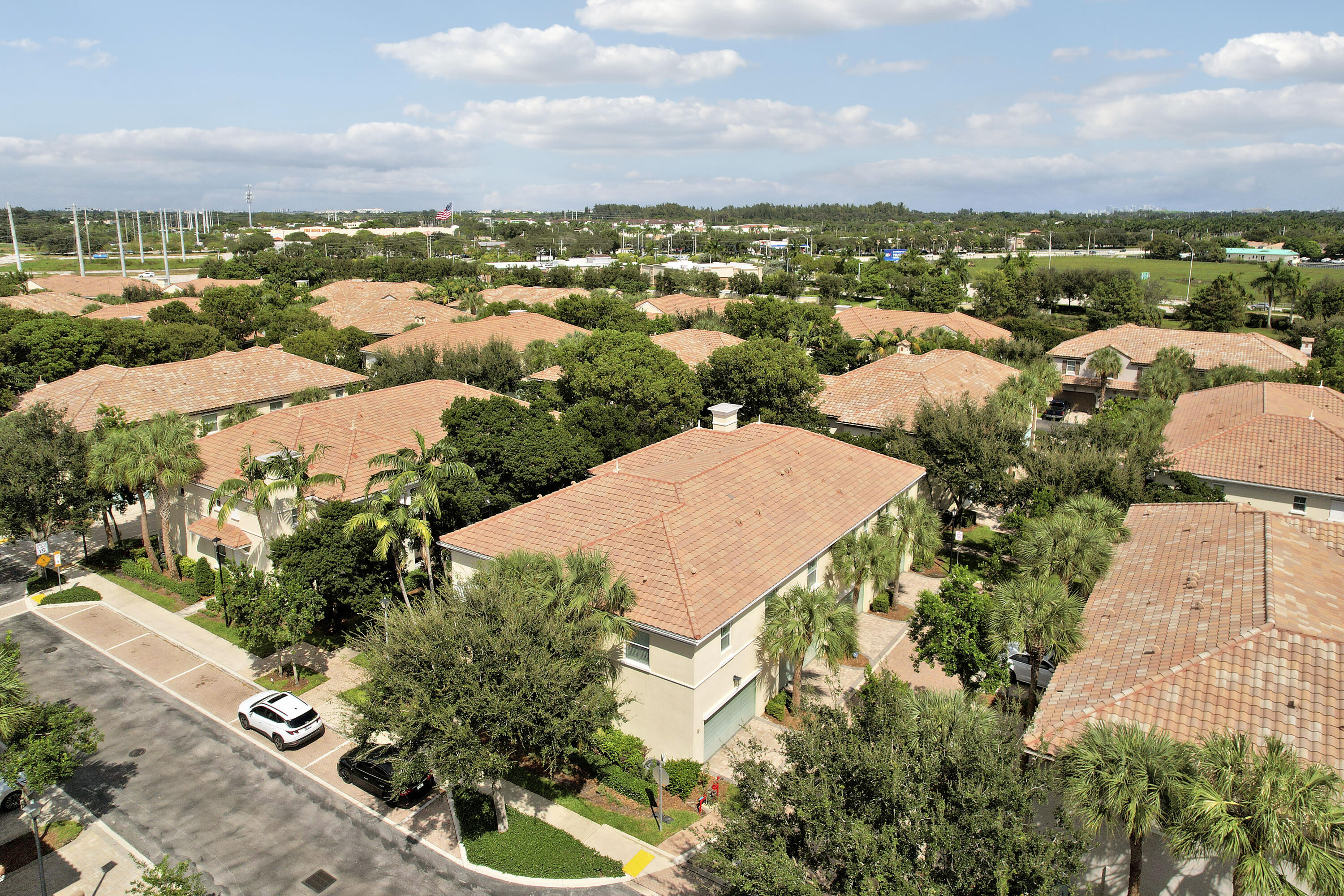 Aerial perspective of multi-unit residential complex featuring terracotta-style roof tiles, light-toned stucco facades, paver-stone driveways, and mature palms and shade trees throughout the grounds Aerial perspective of multi-unit residential complex featuring terracotta-style roof tiles, light-toned stucco facades, paver-stone driveways, and mature palms and shade trees throughout the grounds