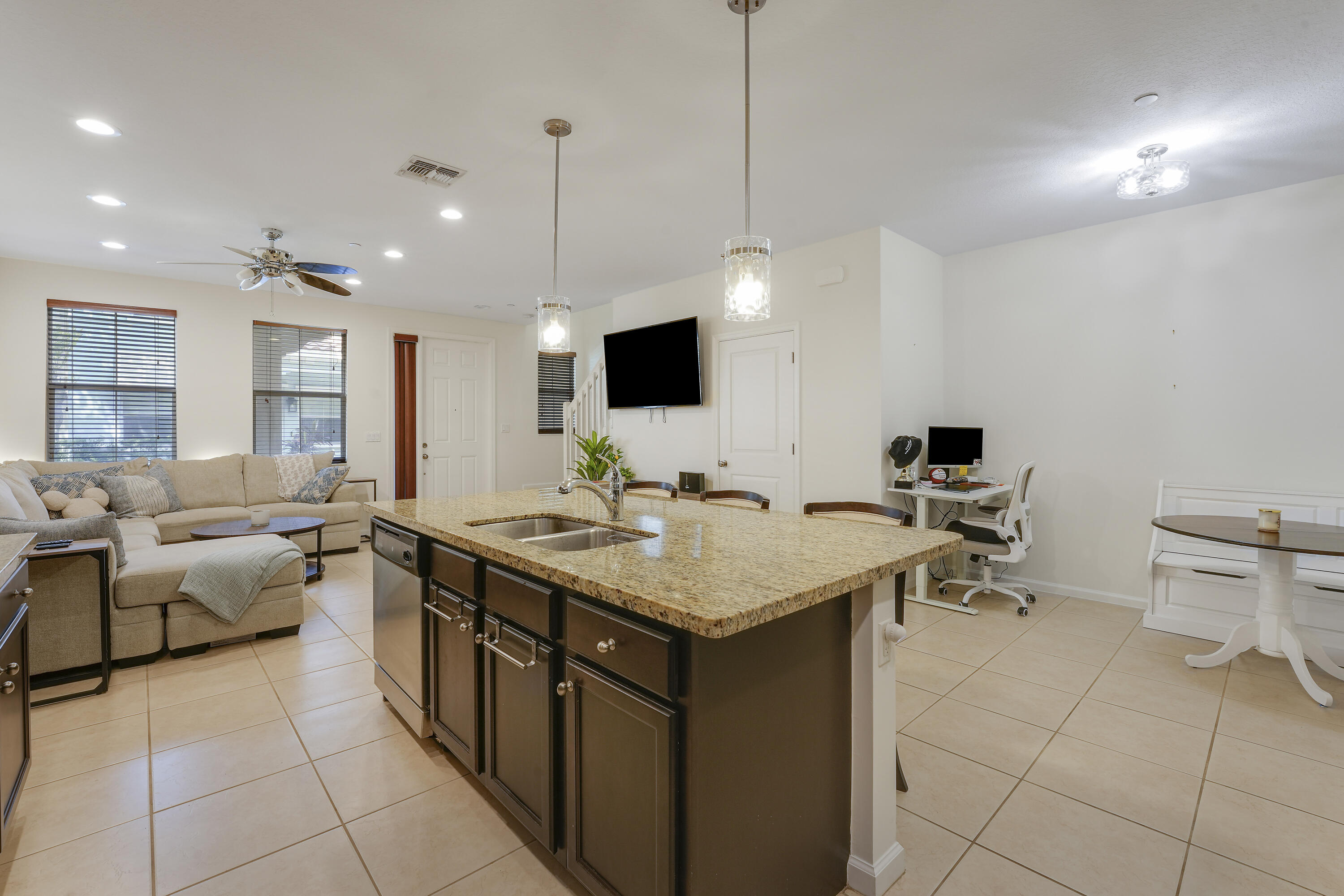 Kitchen featuring a central island with a stone countertop, dual-basin stainless steel sink, dark-finish cabinetry, stainless steel dishwasher, and dual pendant lighting
