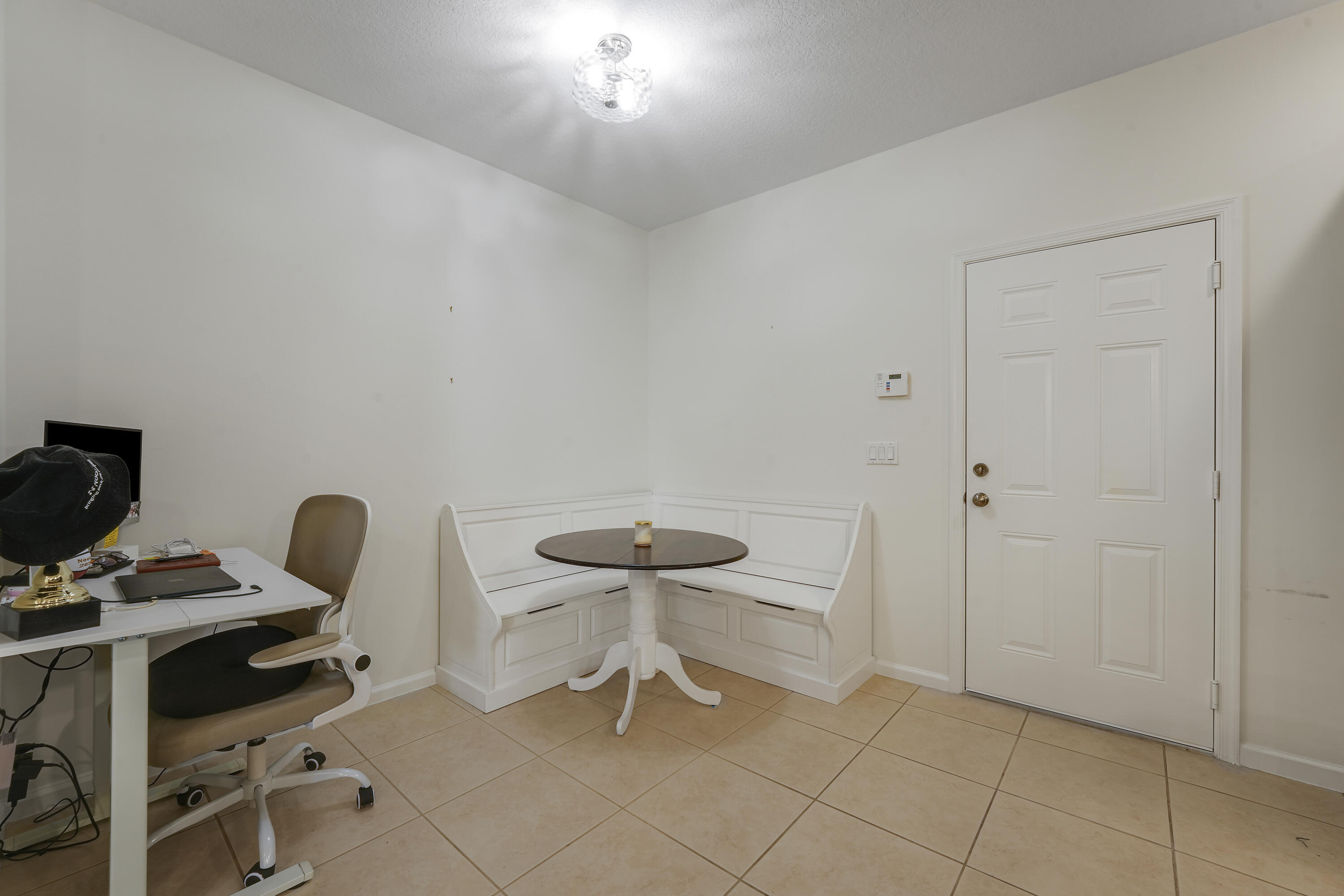 Built-in white corner bench seating, neutral tile flooring, multi-panel entry door, and flush-mount ceiling light fixture