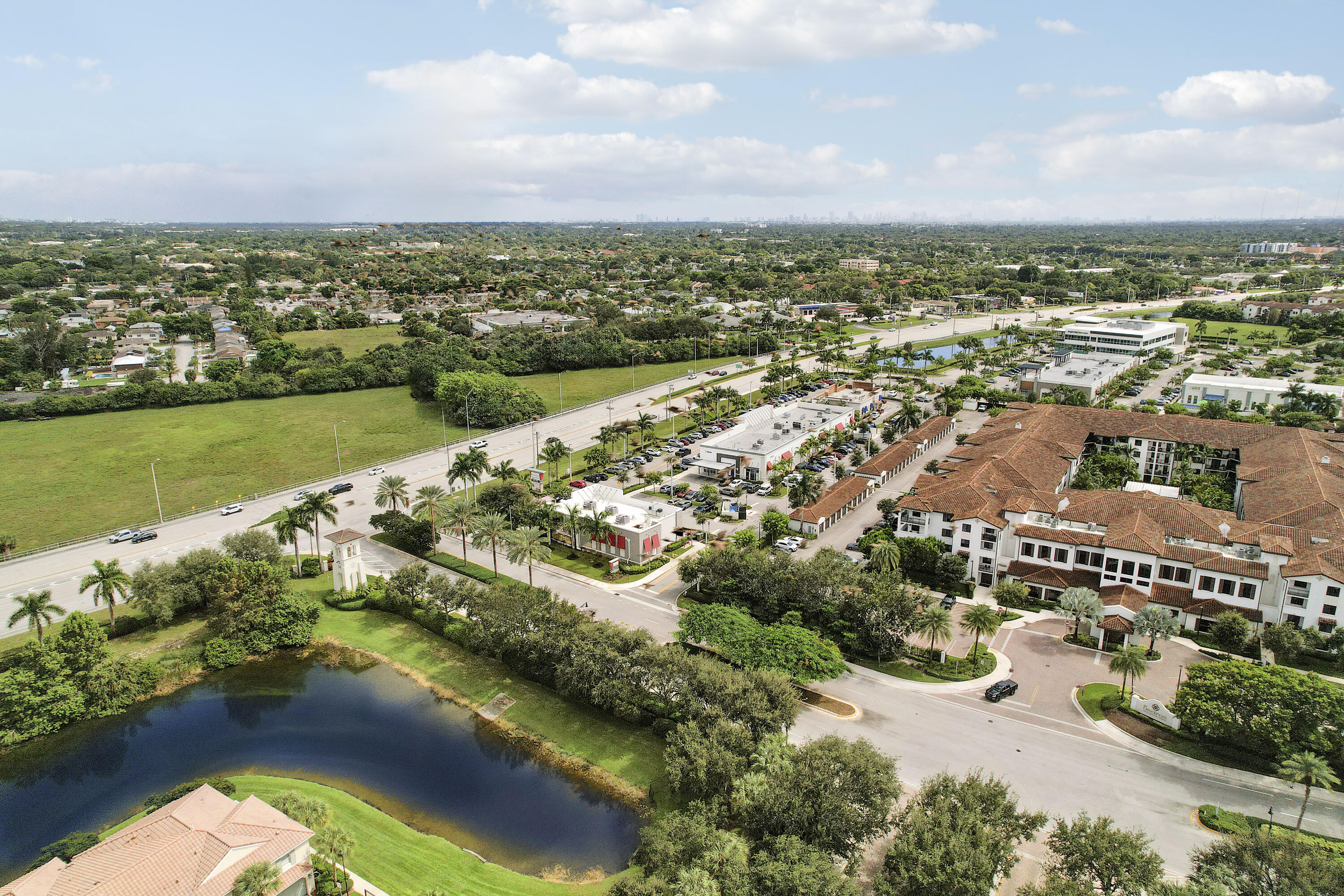 Aerial perspective featuring a multi-story building with a clay tile roof, a central courtyard, and a prominent water feature surrounded by established palm trees and manicured landscaping