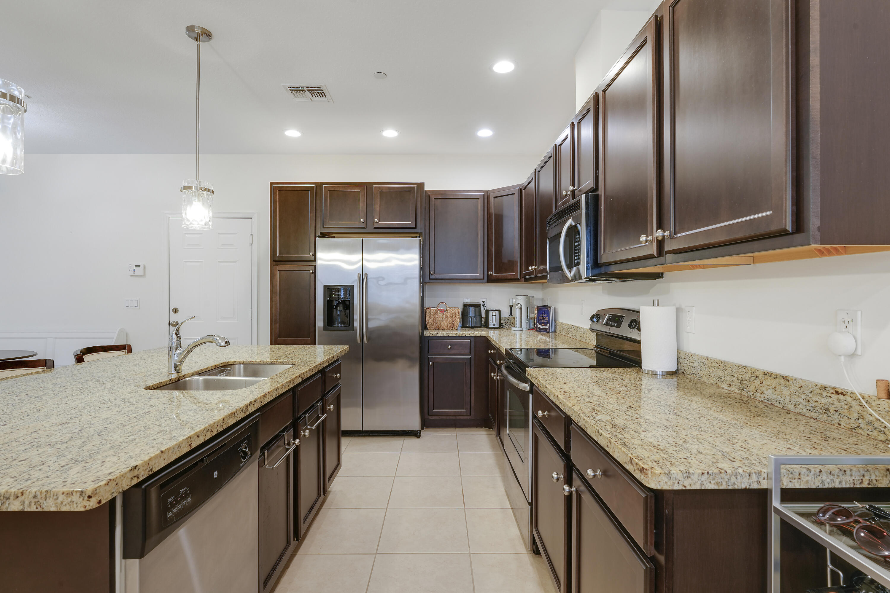 Kitchen featuring dark-finish cabinetry, stone-surface countertops, stainless steel appliances, a center island with a dual-basin sink, and recessed lighting