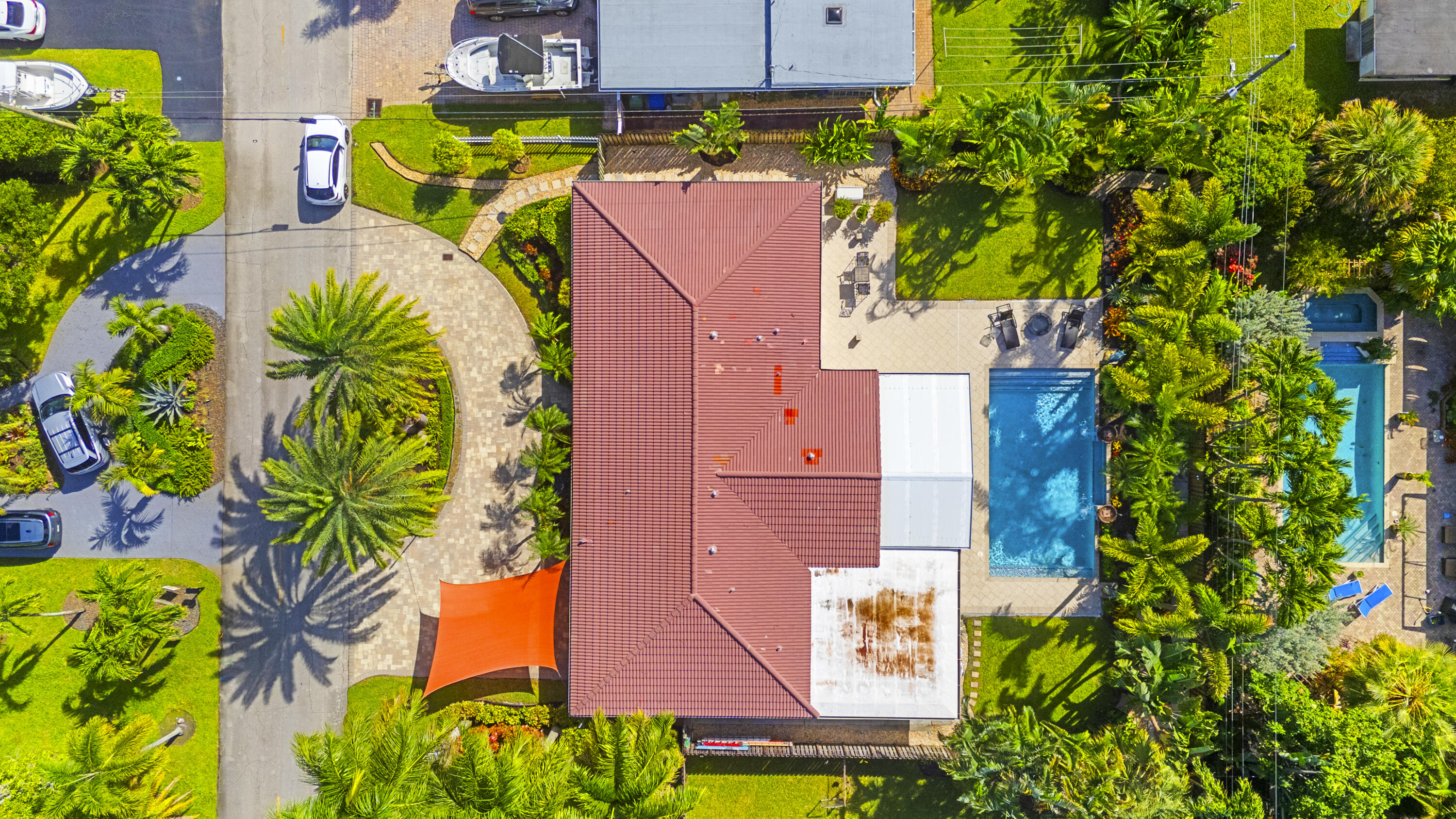Aerial perspective featuring a tile roof, paved circular driveway, swimming pool, and extensive mature landscaping