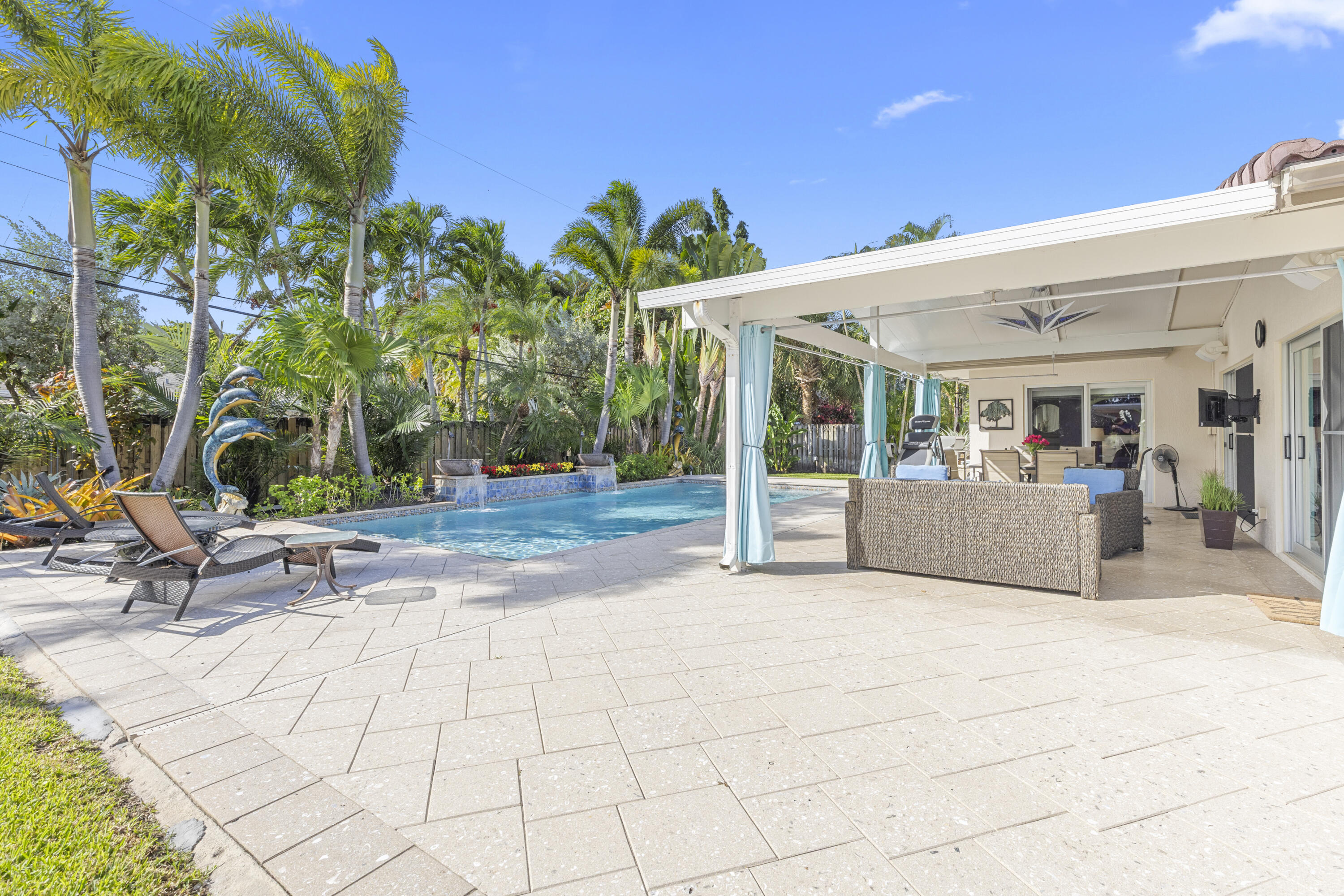 Covered patio with paver flooring, swimming pool featuring a decorative water feature, and mature palm trees