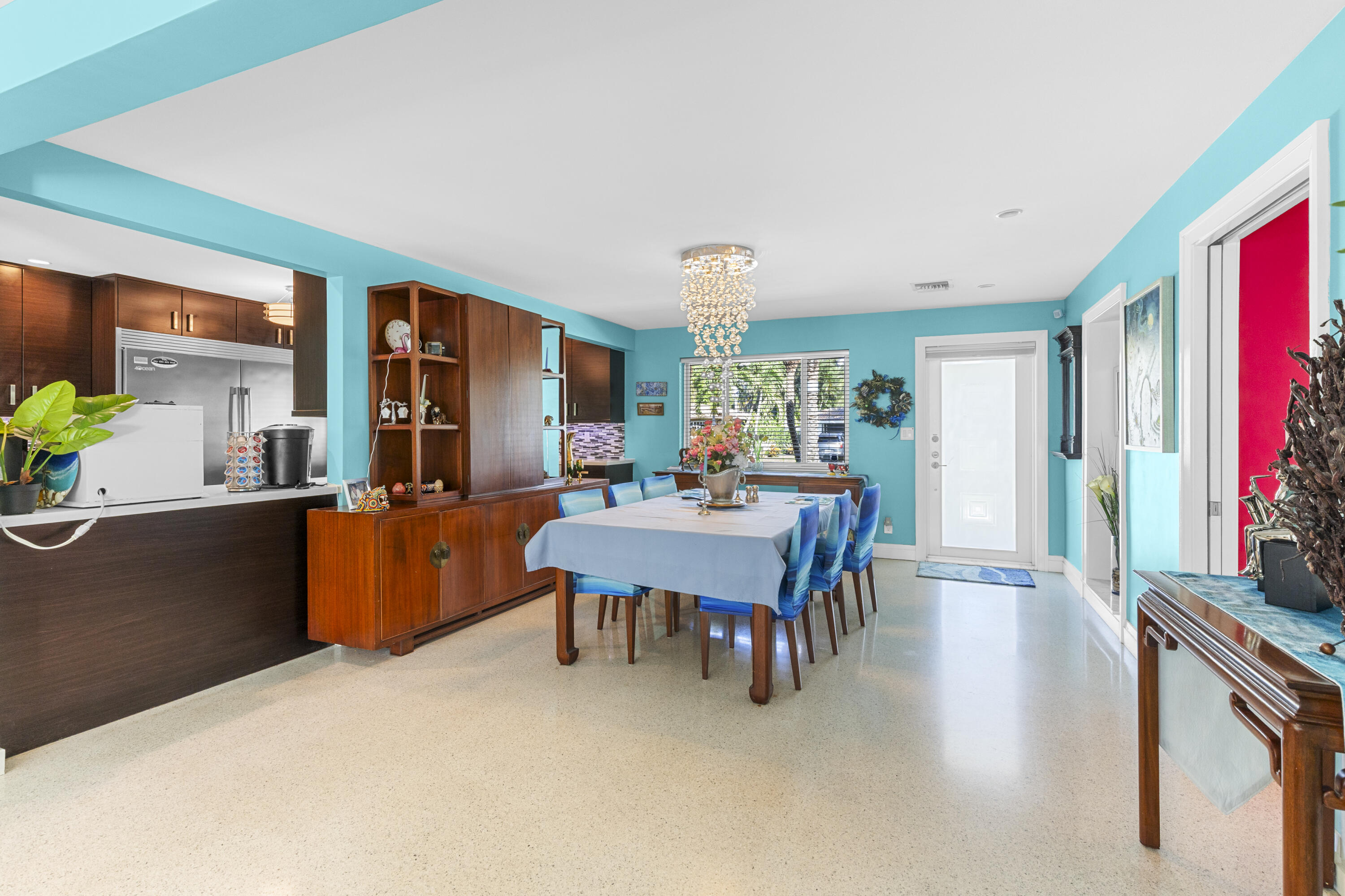 Open-concept dining area featuring terrazzo flooring, built-in mahogany cabinetry, a crystal chandelier, and large window