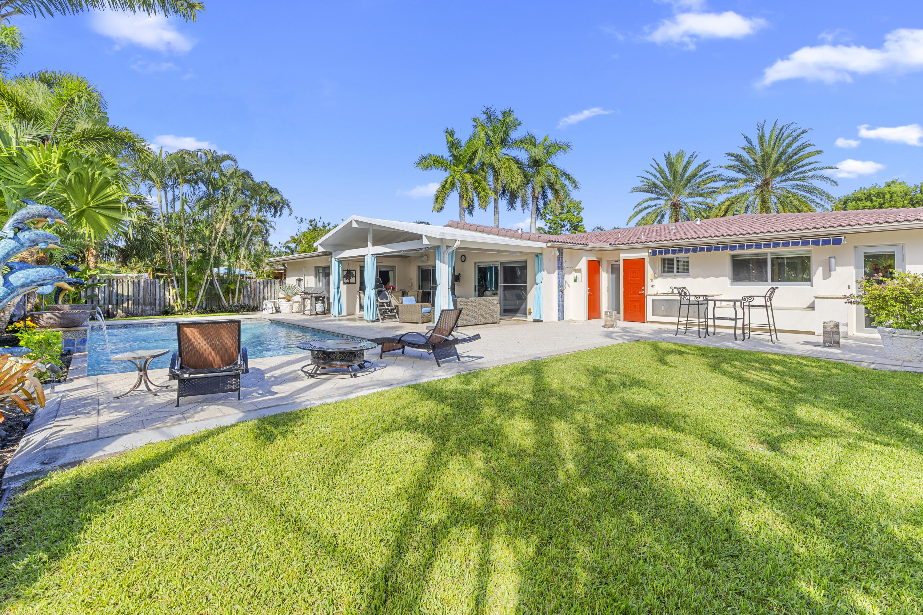 Backyard featuring a concrete pool deck, in-ground swimming pool, covered patio, manicured lawn, and mature palm trees