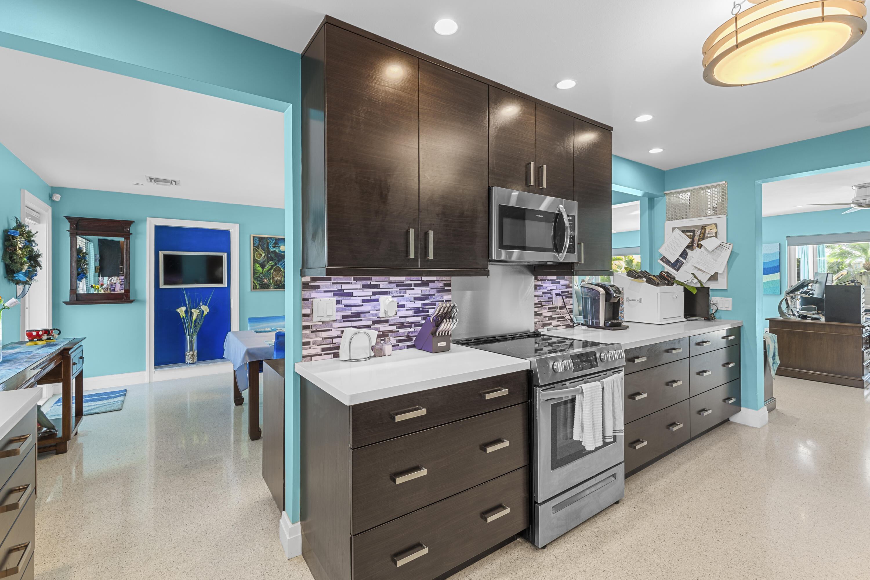 Kitchen featuring dark wood-finish cabinetry, quartz countertops, stainless steel appliances, a multi-toned tile backsplash, and recessed lighting