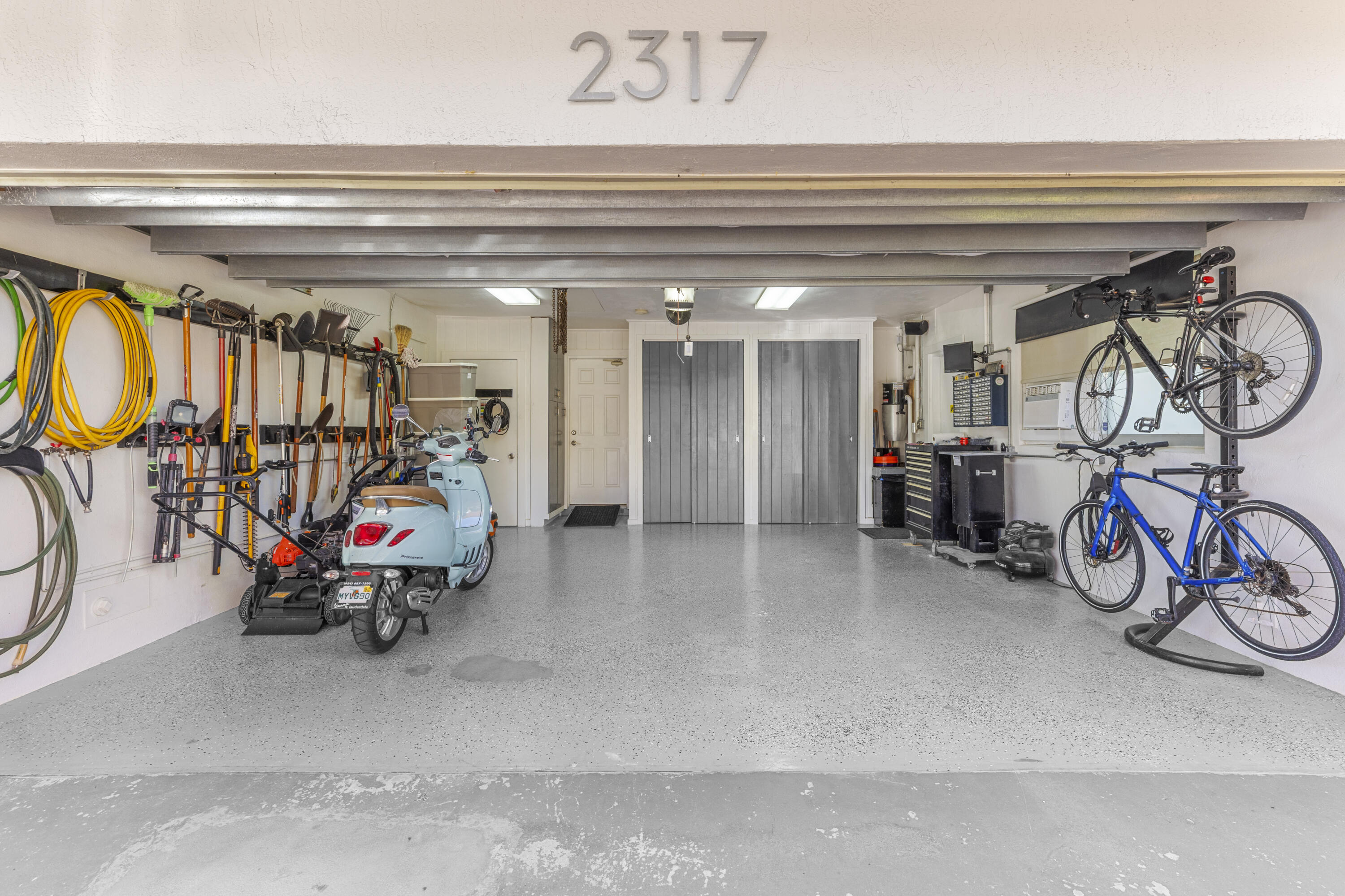 Attached two-car garage featuring epoxy-coated flooring, overhead fluorescent lighting, built-in wall-mounted organizational tracks, and dual floor-to-ceiling storage closets