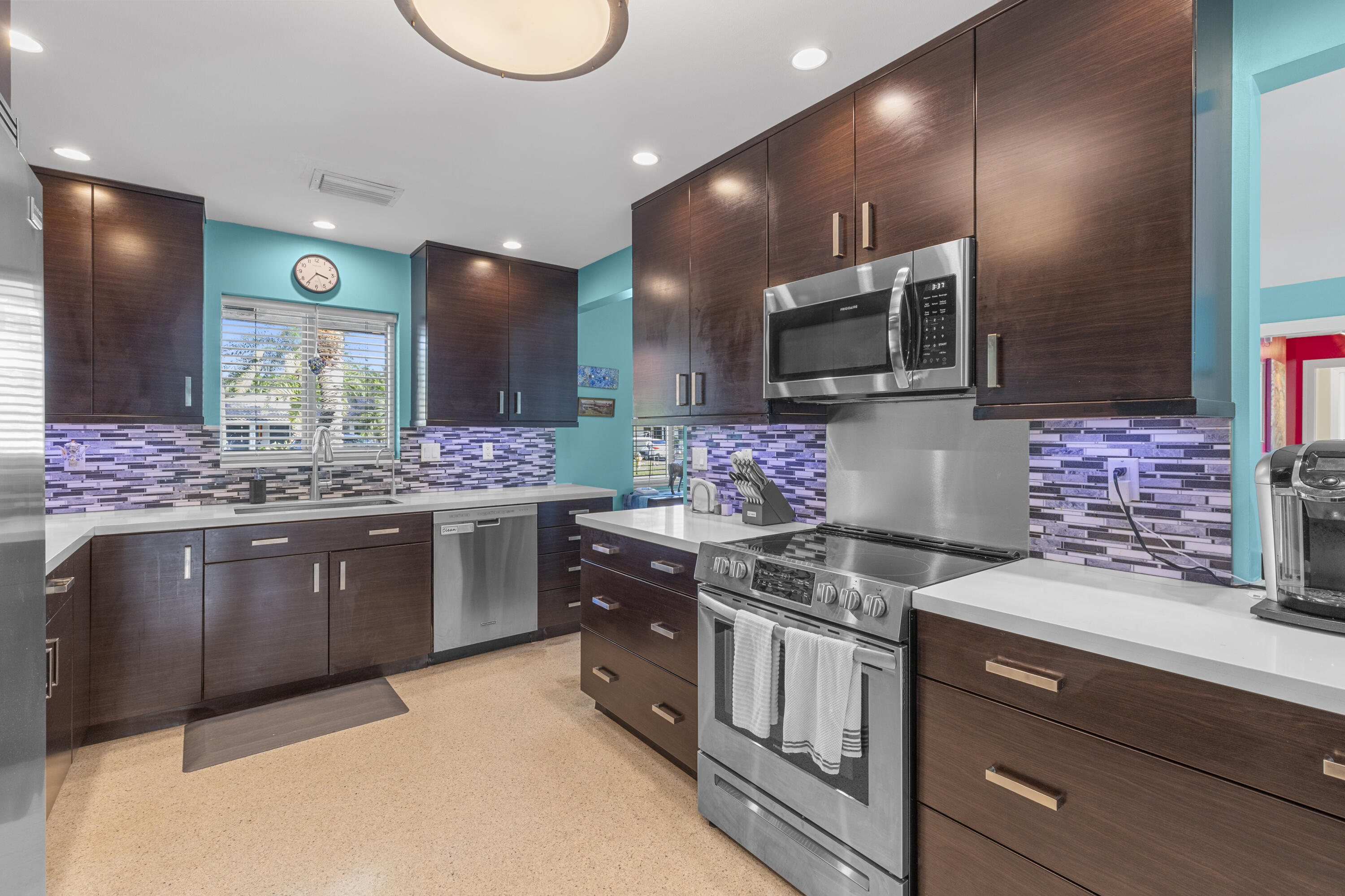 Dark wood-finish cabinetry, stainless steel appliances, multi-colored glass tile backsplash, quartz countertops, and recessed lighting