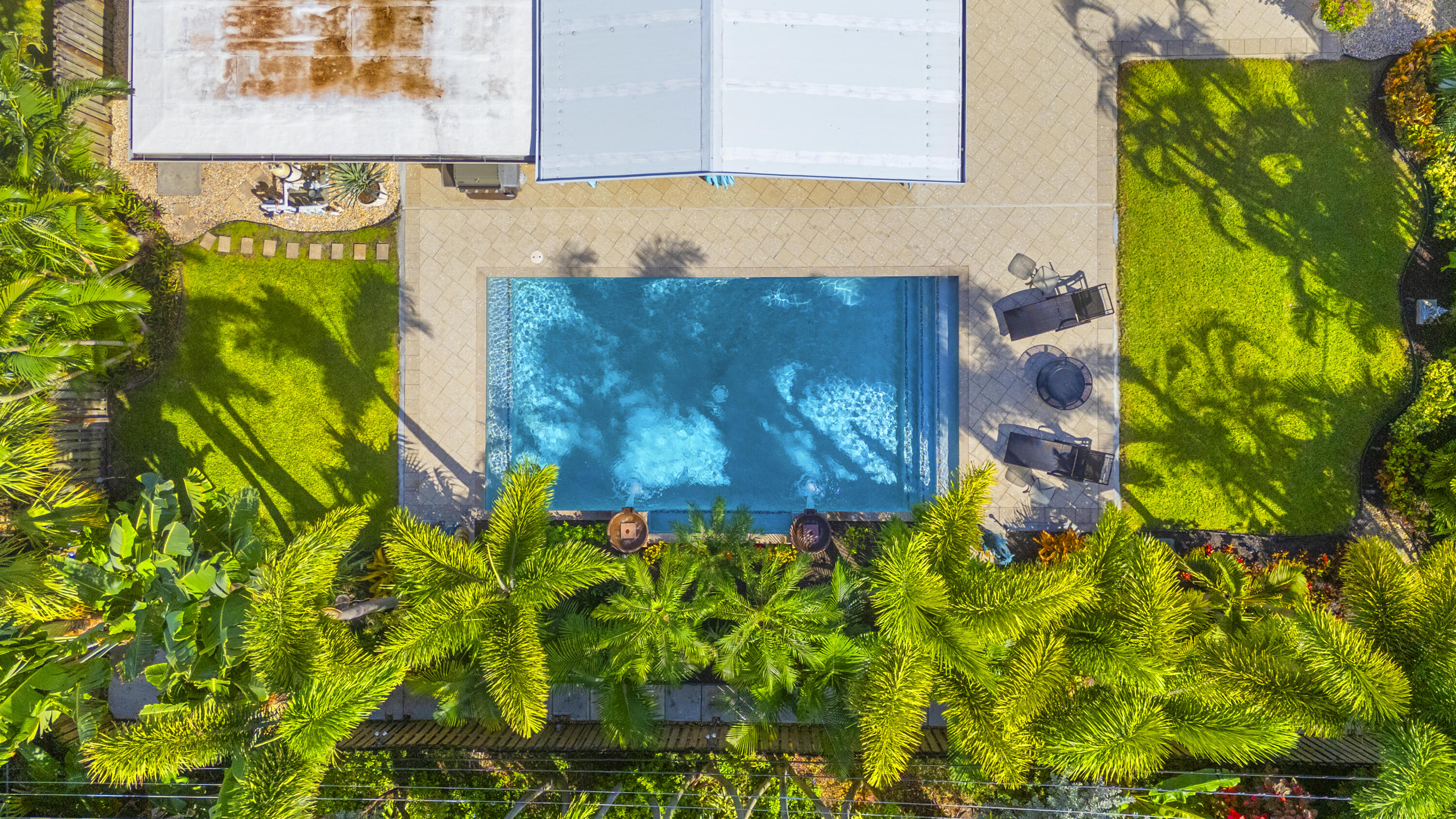 Backyard featuring a rectangular swimming pool, concrete paver decking, manicured lawn areas, and mature perimeter landscaping