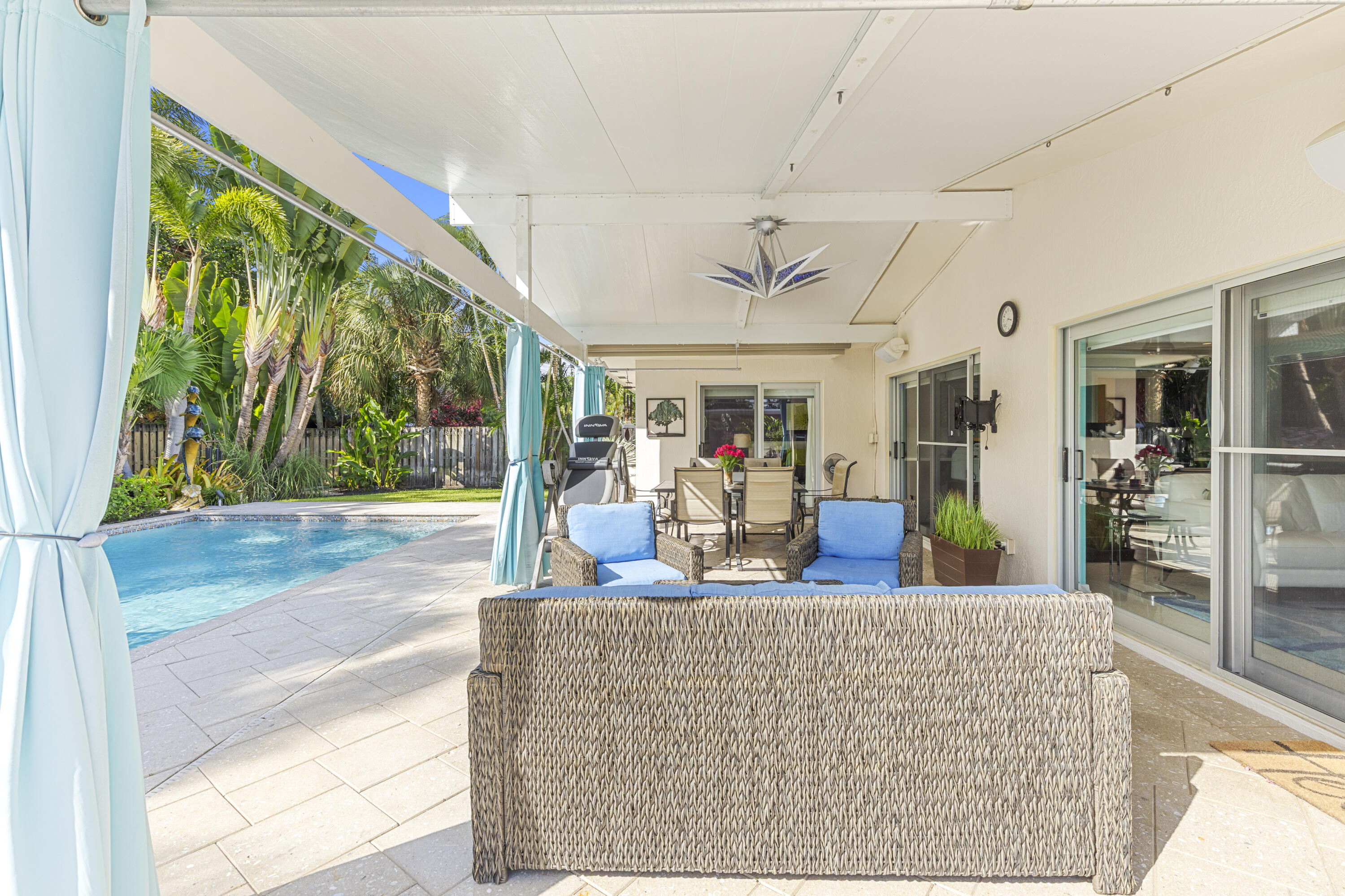 Covered patio featuring a paved stone deck, ceiling-mounted lighting fixture, and sliding glass door access, complemented by an inground swimming pool and privacy fencing