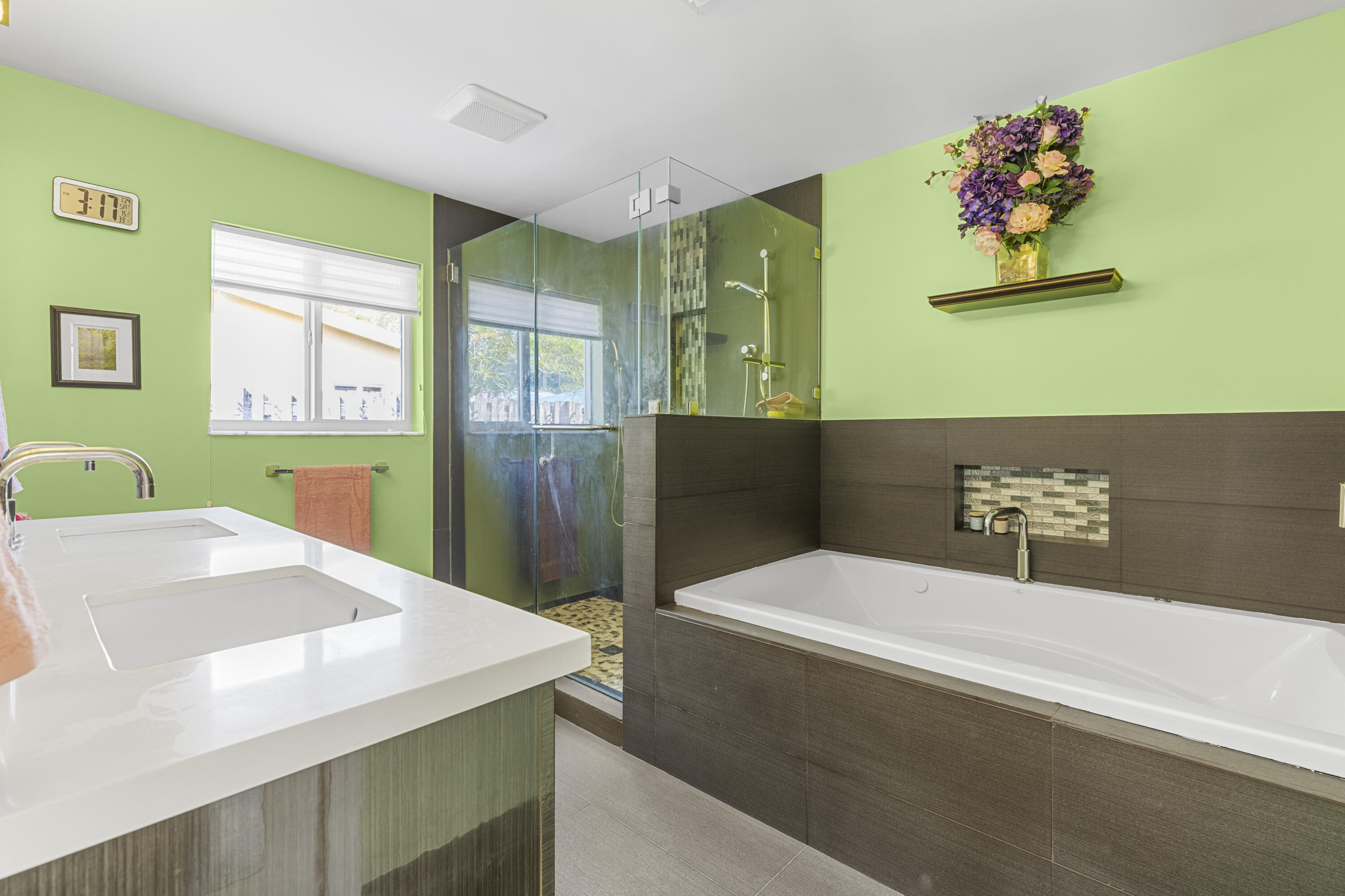 Dual vanity with rectangular undermount sinks and white solid-surface countertops, walk-in shower with glass enclosure, and built-in soaking tub featuring a tiled niche and surround