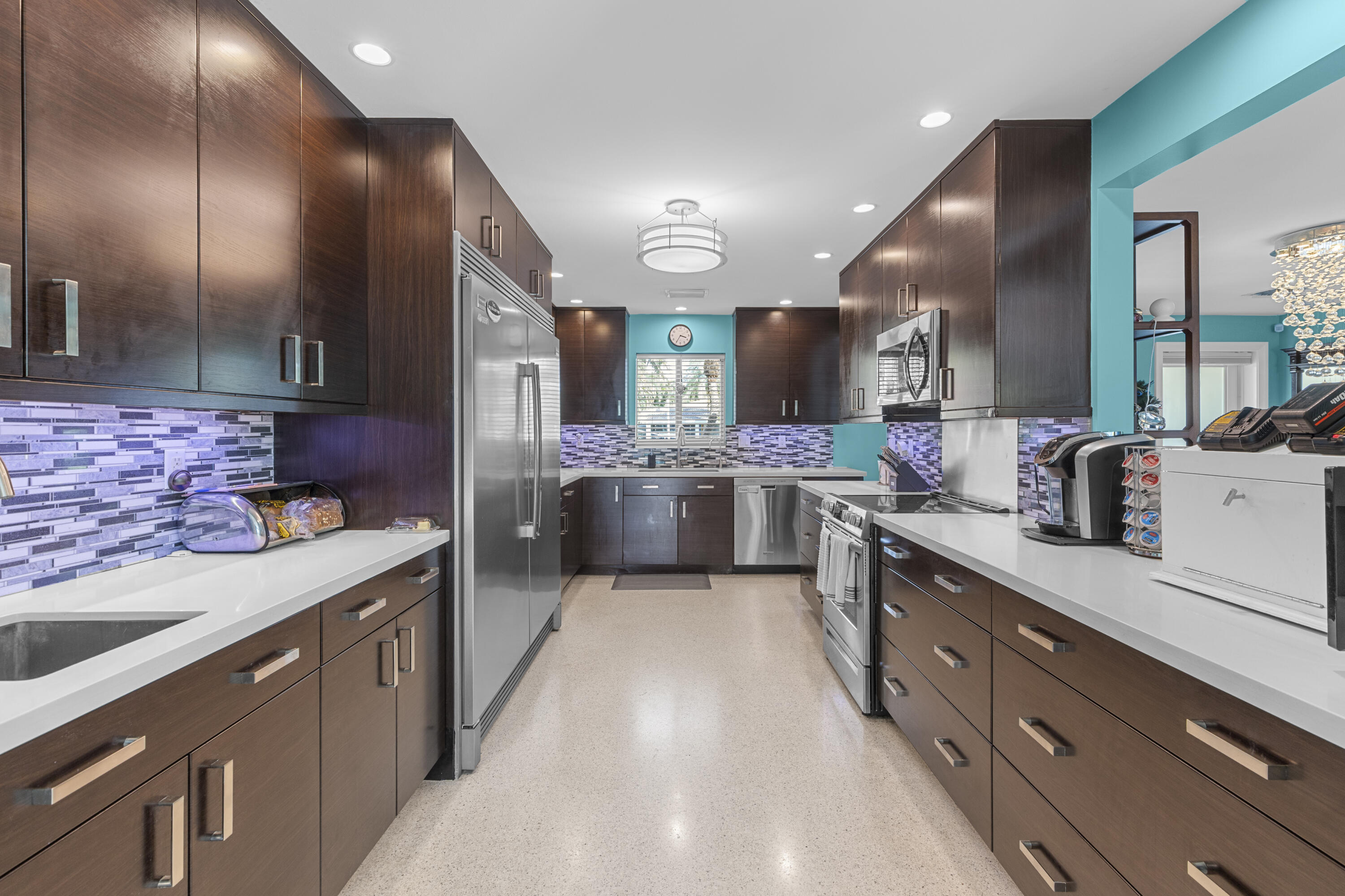 Kitchen featuring dark wood cabinetry, light-toned solid surface countertops, a mosaic tile backsplash, stainless steel appliances, and recessed lighting