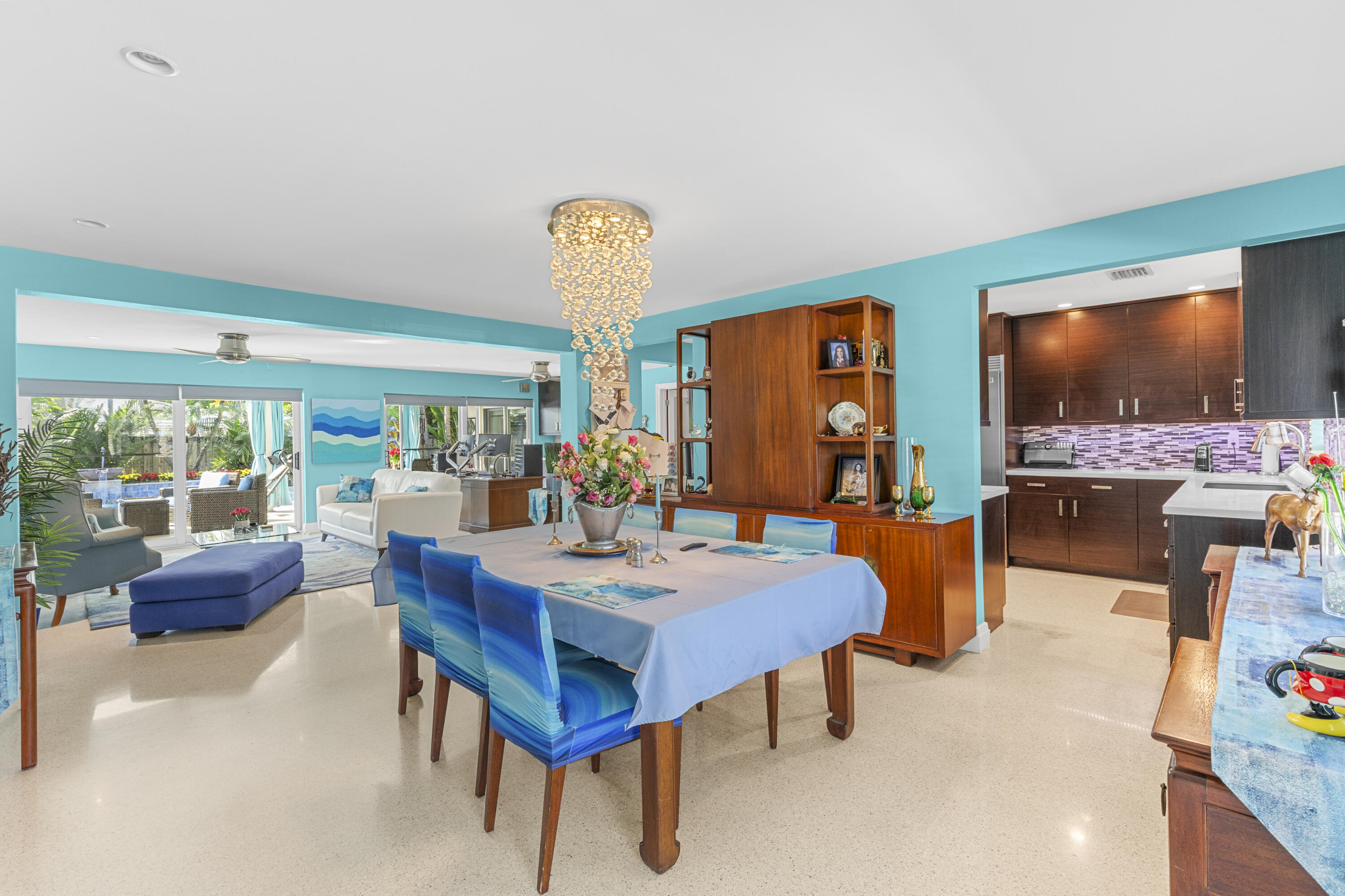 Open-concept interior featuring light-reflecting terrazzo flooring, custom built-in wood cabinetry, recessed lighting, and a tiered crystal chandelier