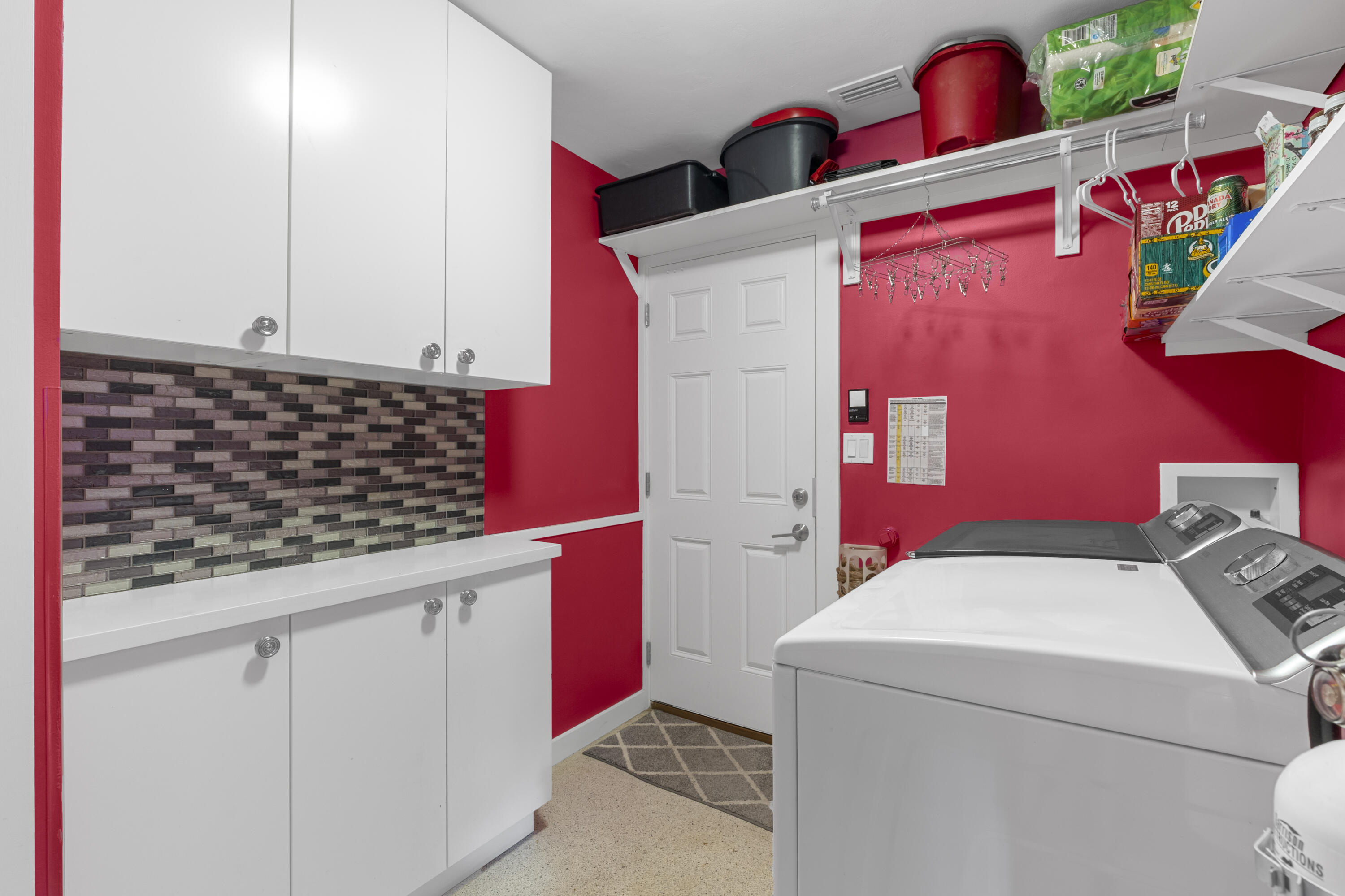 Laundry area featuring white cabinetry, a solid-surface countertop, decorative tile backsplash, and open shelving