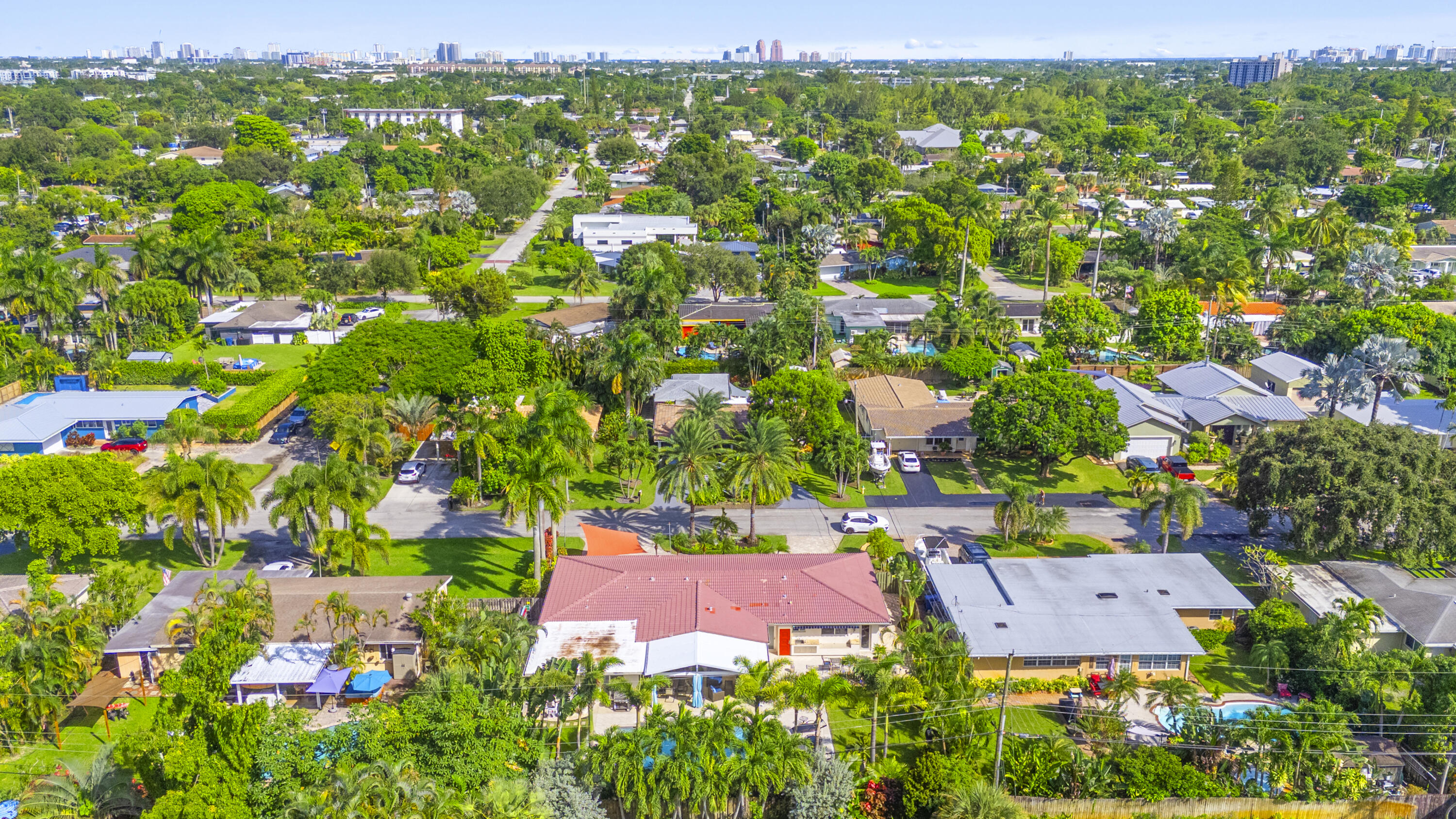 Aerial perspective of a property featuring a red metal roof, expansive lawn, mature landscaping, and a fenced backyard
