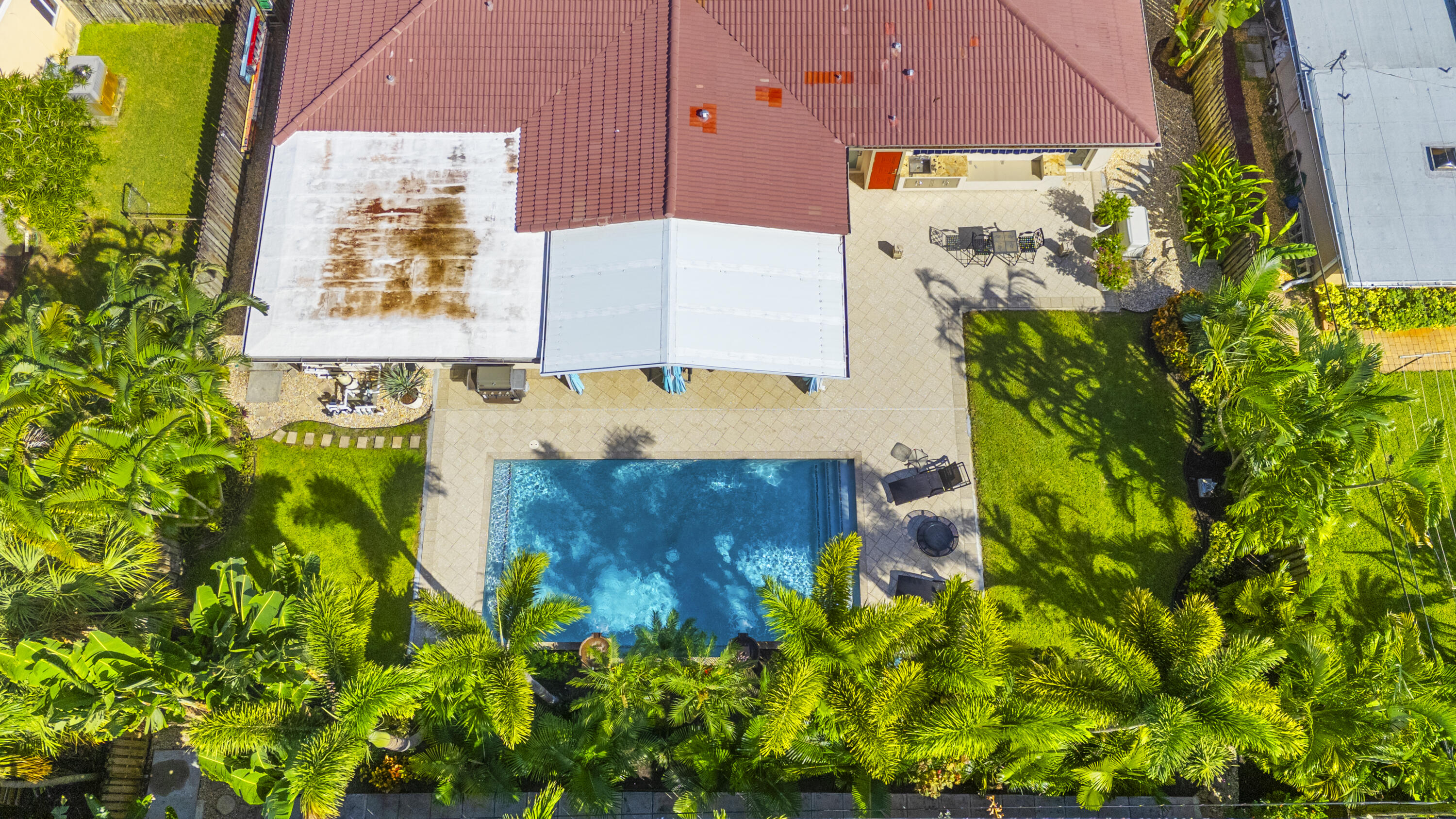 Aerial view of the backyard featuring a rectangular swimming pool, expansive paved patio, covered porch, and mature perimeter landscaping