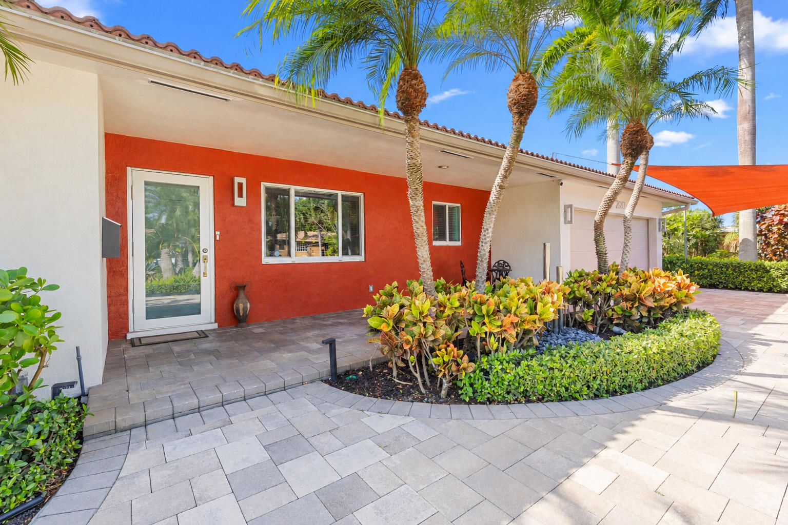 Stucco exterior with contrasting masonry finishes, paved hardscaping, landscaped garden beds, and palm trees