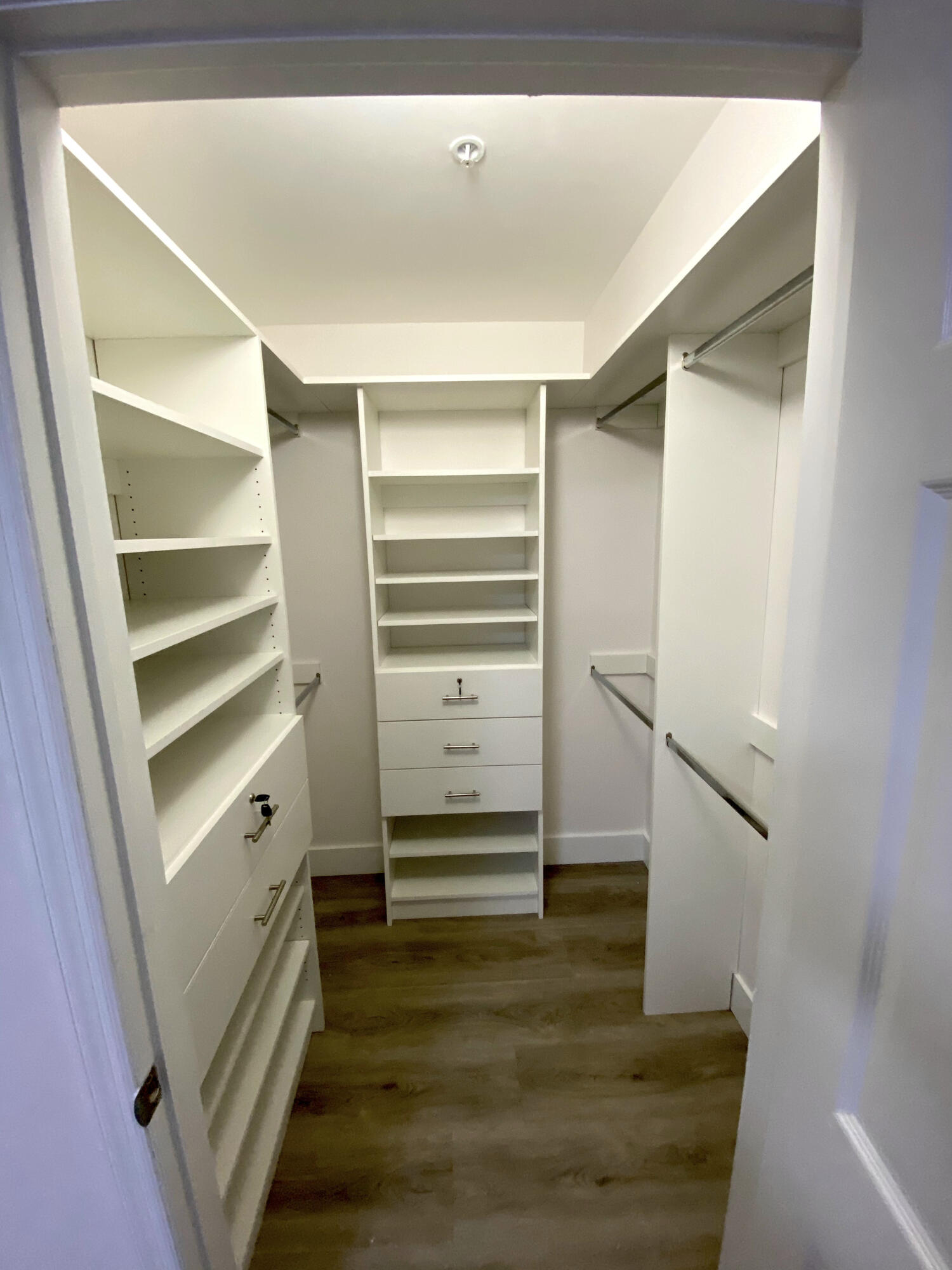 Walk-in closet featuring white custom built-in shelving, multi-drawer storage units with integrated locks, wood-finish flooring, and dual-level metal hanging rods